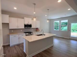 Modern kitchen with white cabinets, quartz island, and stainless steel appliances in The Willow C, Woodland Crossing home.