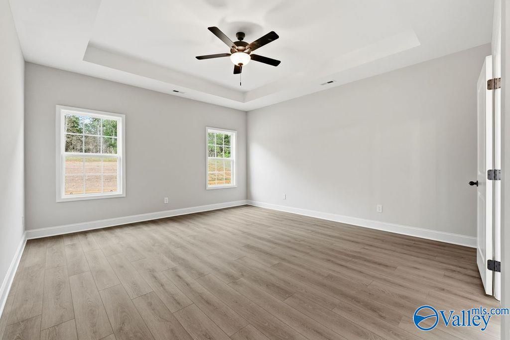 Empty bedroom with tray ceiling, ceiling fan, large windows, and hardwood floors in Davidson Homes The Rockford B, Hartselle, Alabama