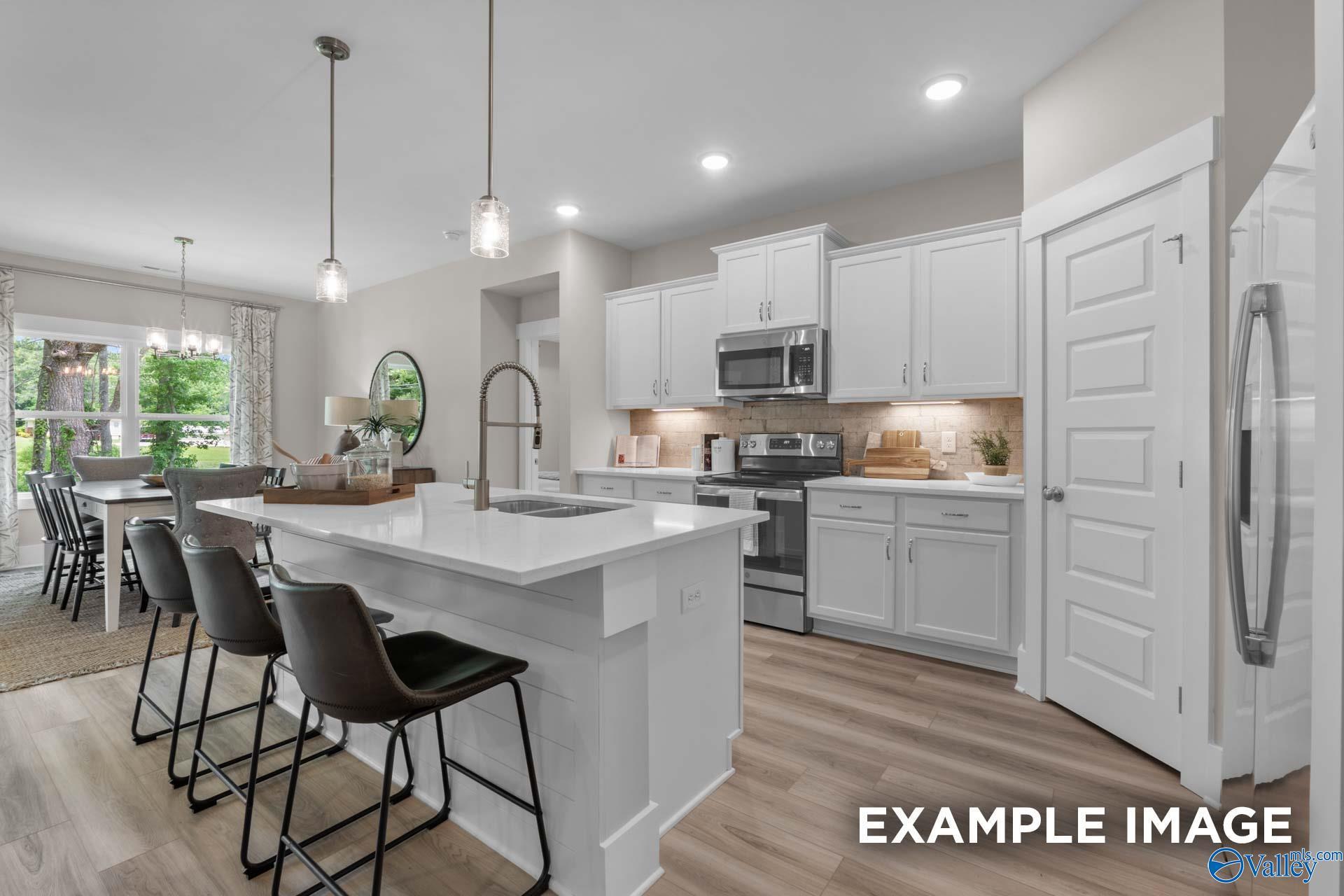 White kitchen with island, quartz countertops, stainless appliances, and bar seating in Davidson Homes The Everett B, Little Creek Arab, Alabama