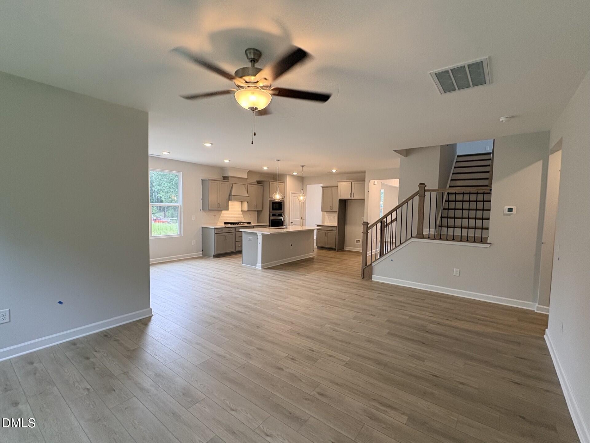 Open-concept kitchen and living area with island, luxury vinyl plank floors, and staircase in Davidson Homes The Ash C, Zebulon NC