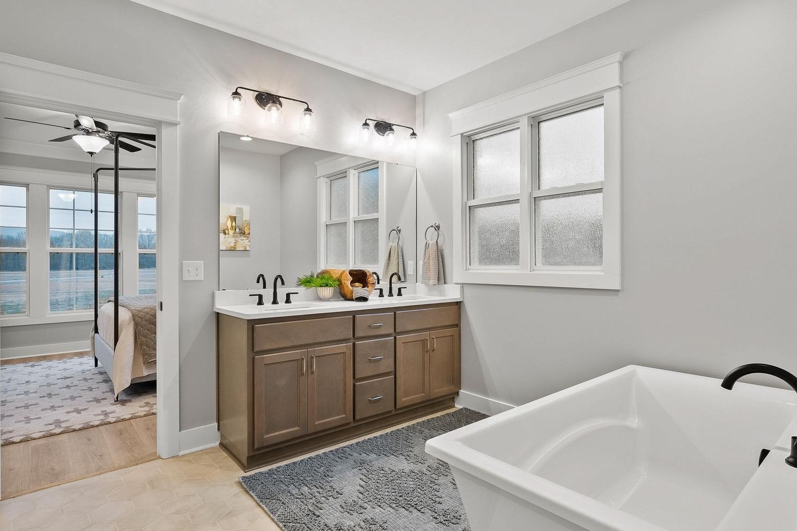 Luxurious master bathroom in The Oxford featuring double vanity, freestanding tub, and adjacent bedroom view