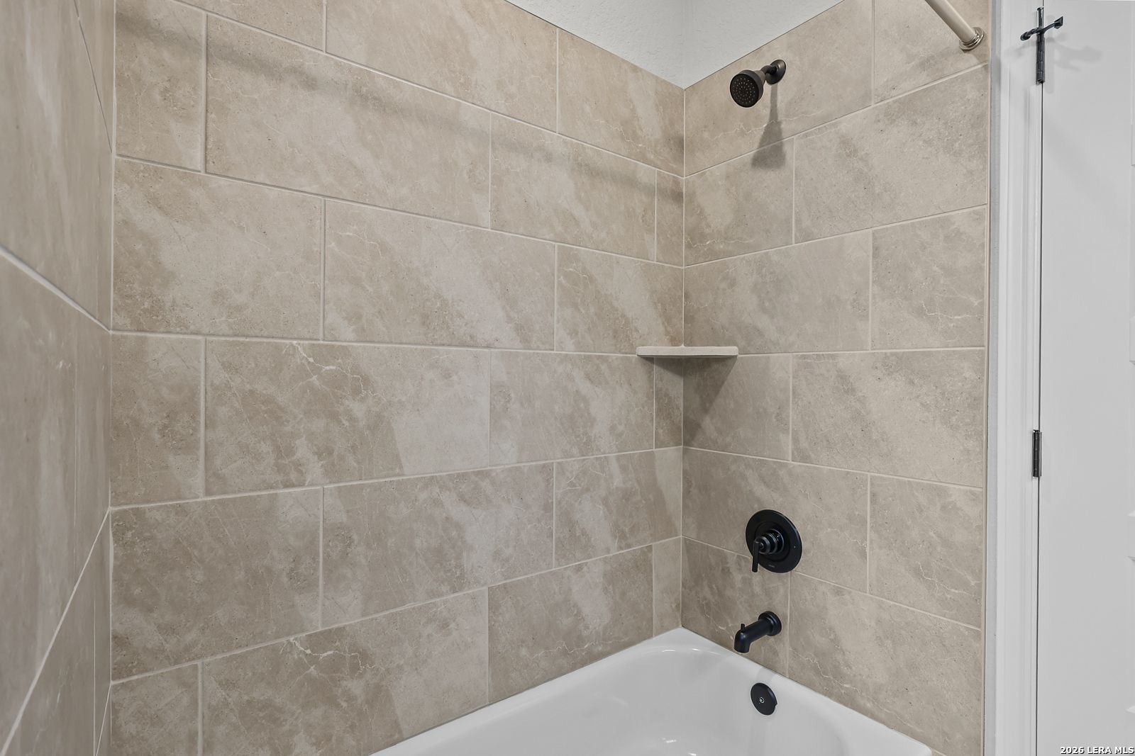 Elegant beige marble-look tiled bathroom with soaking tub, shower, and black fixtures in Davidson Homes The Belmont H, Castroville, Texas
