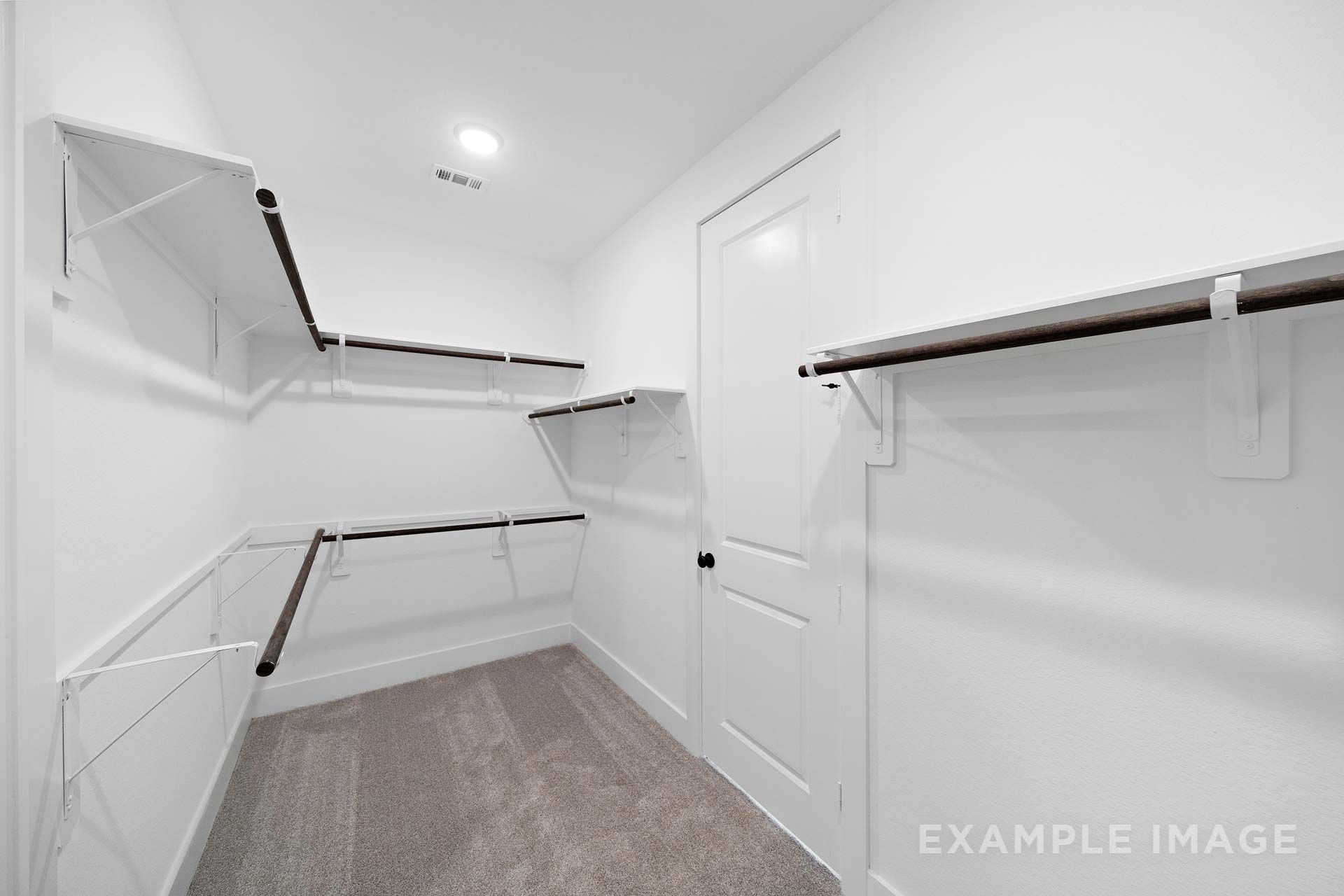 Spacious walk-in closet in The Elizabeth by Davidson Homes featuring white shelving, dark wood hanging rods, and carpet flooring