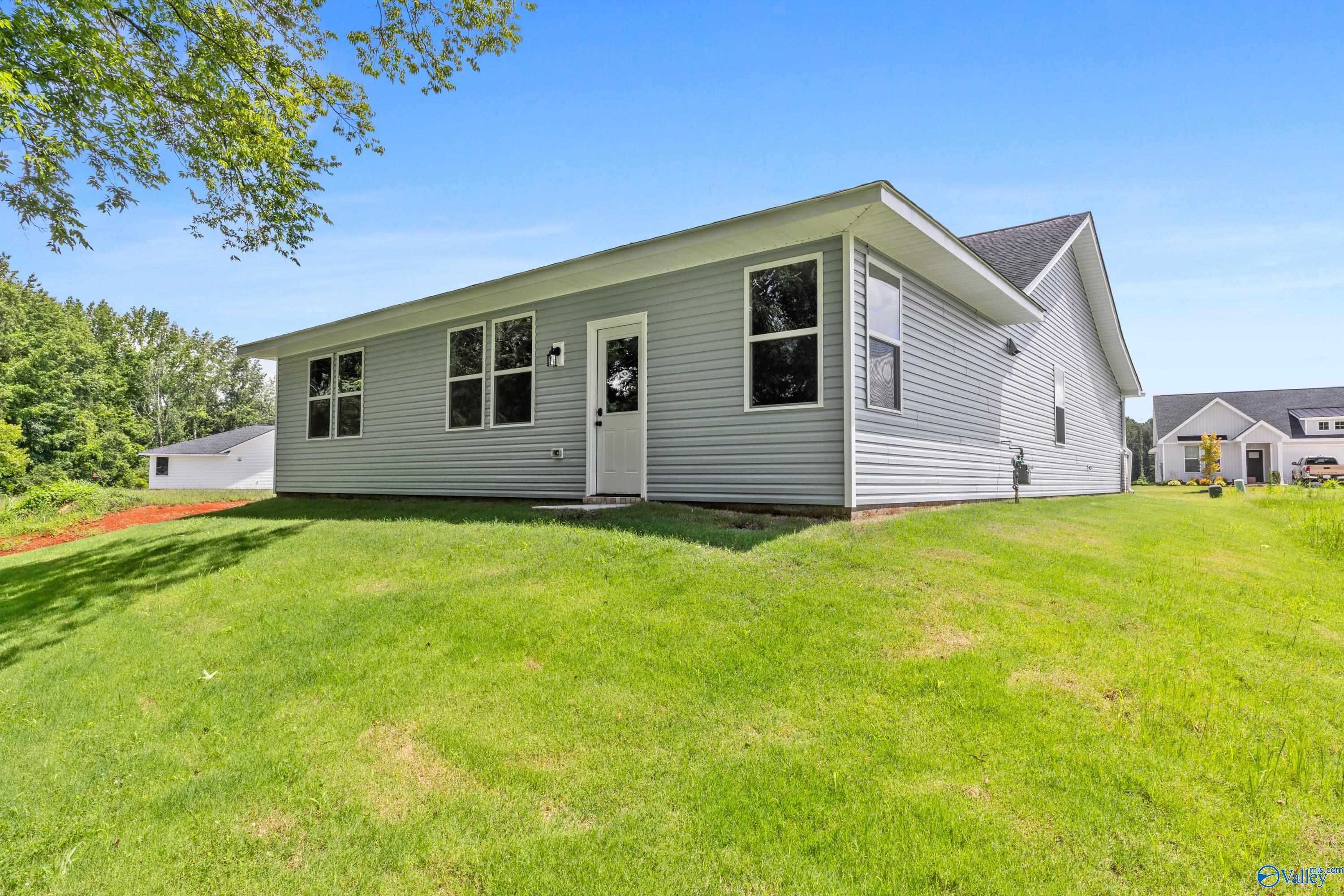 Rear view of gray single-story Phoenix home with back door, large windows, and lush green yard in Forest Glen, Hazel Green, Alabama
