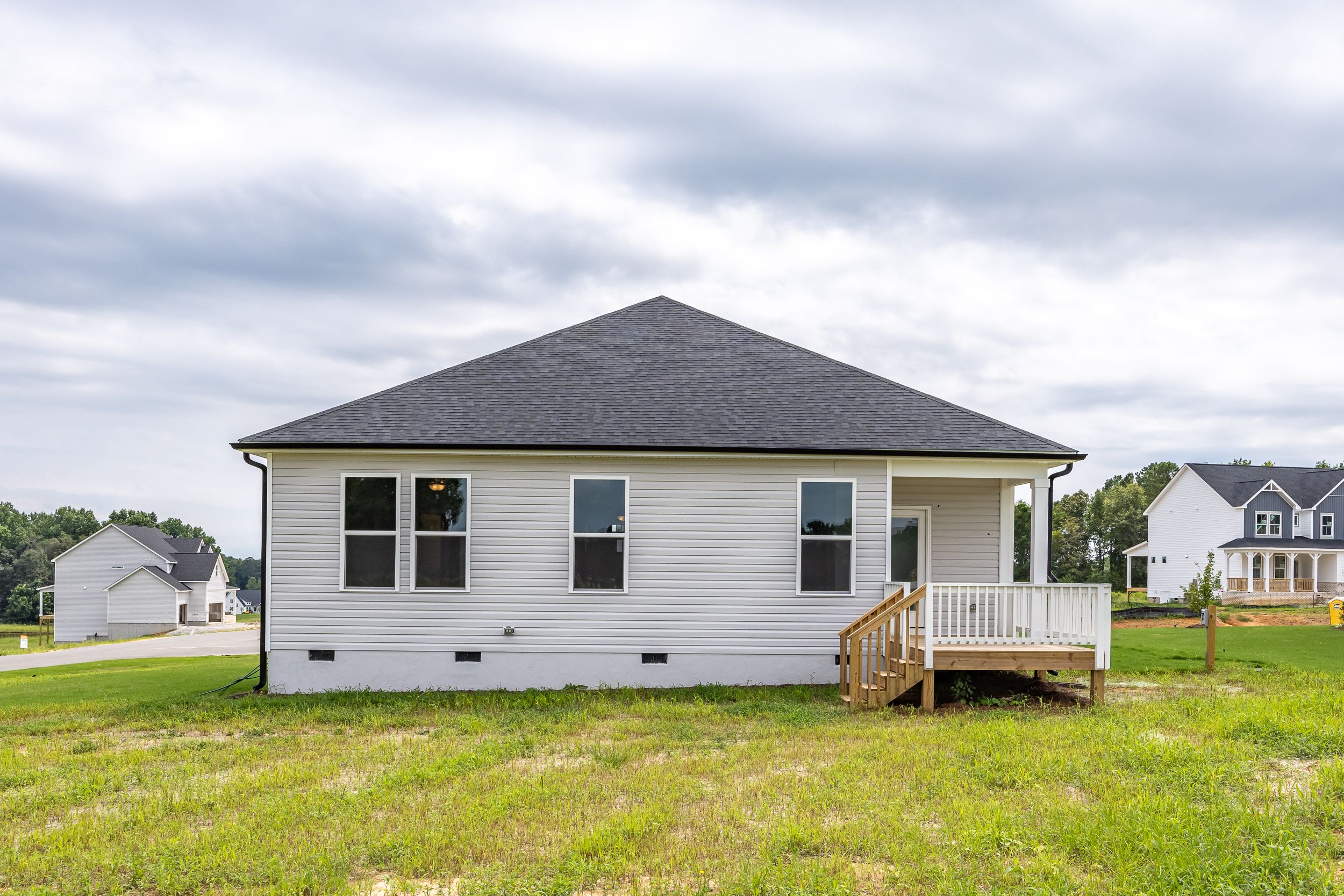 Side elevation of The Daphne C 1-story home featuring white siding, black gable roof, covered porch, and windows in Mooresville NC neighborhood
