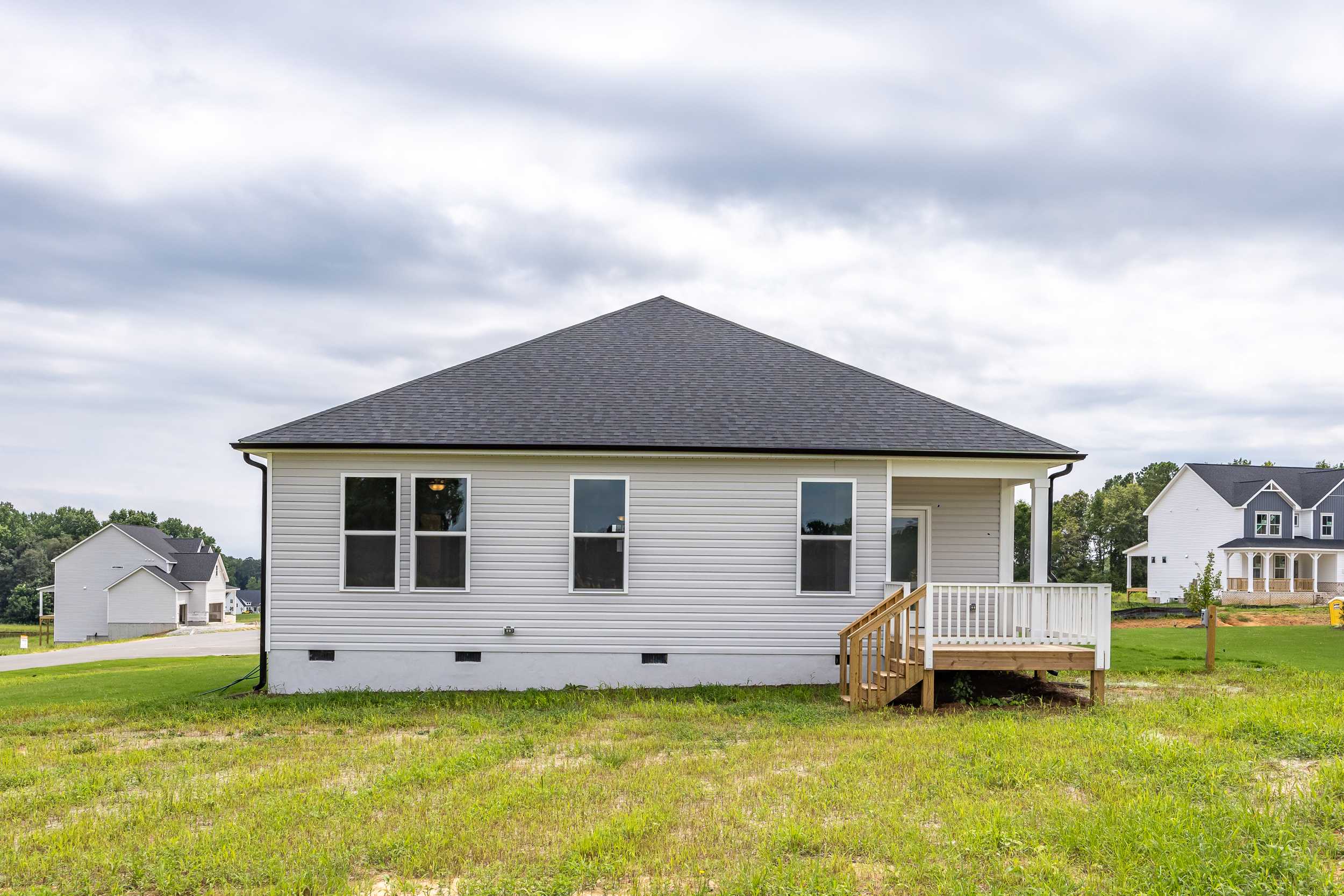 Side elevation of The Daphne C 1-story home featuring white siding, black gable roof, covered porch, and windows in Mooresville NC neighborhood