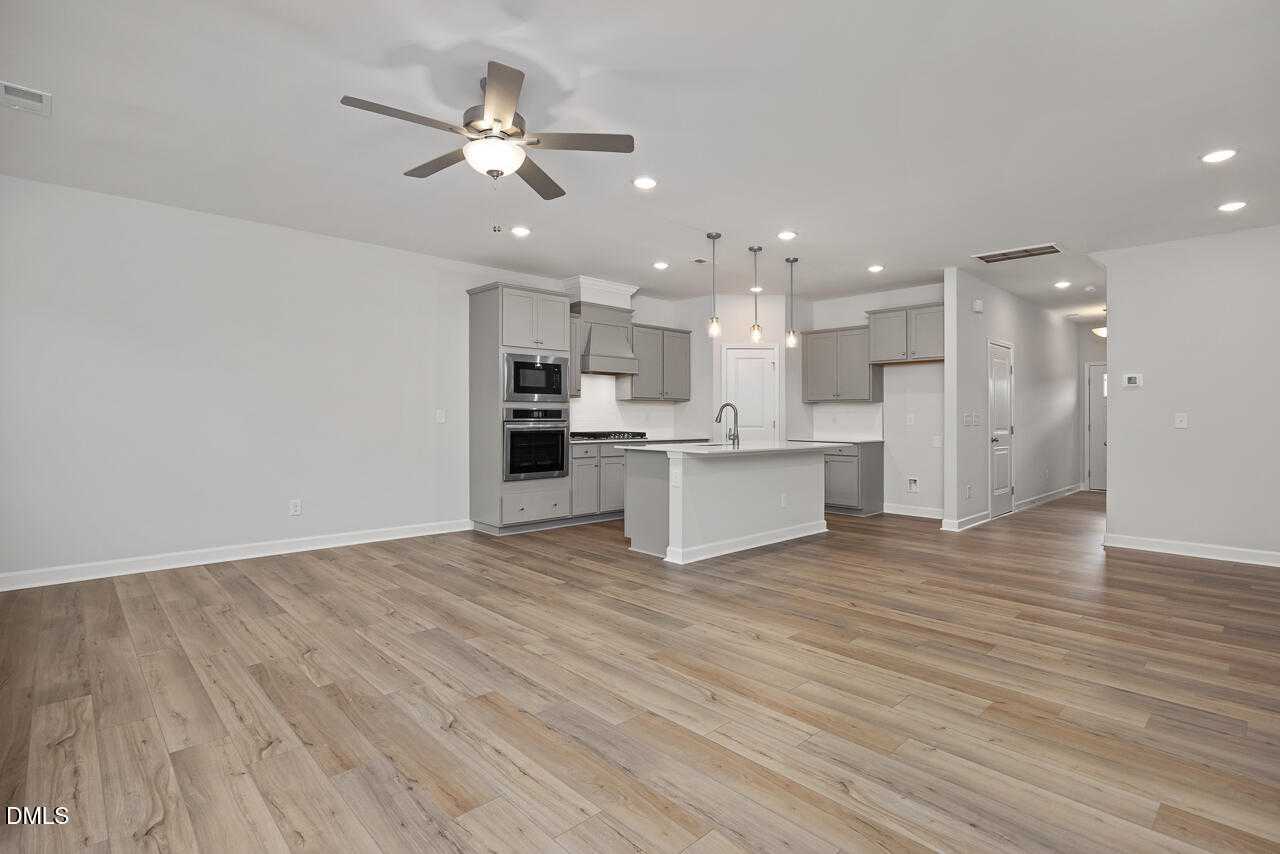 Modern open-concept kitchen with white shaker cabinets, large island sink, double oven, and ceiling fan in Davidson Homes The Warren, Fuquay-Varina, NC
