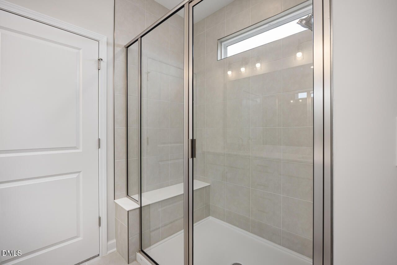 Frameless glass shower with tiled walls, bench seat, and frosted window in master bathroom of The Daphne C by Davidson Homes, Lillington, NC