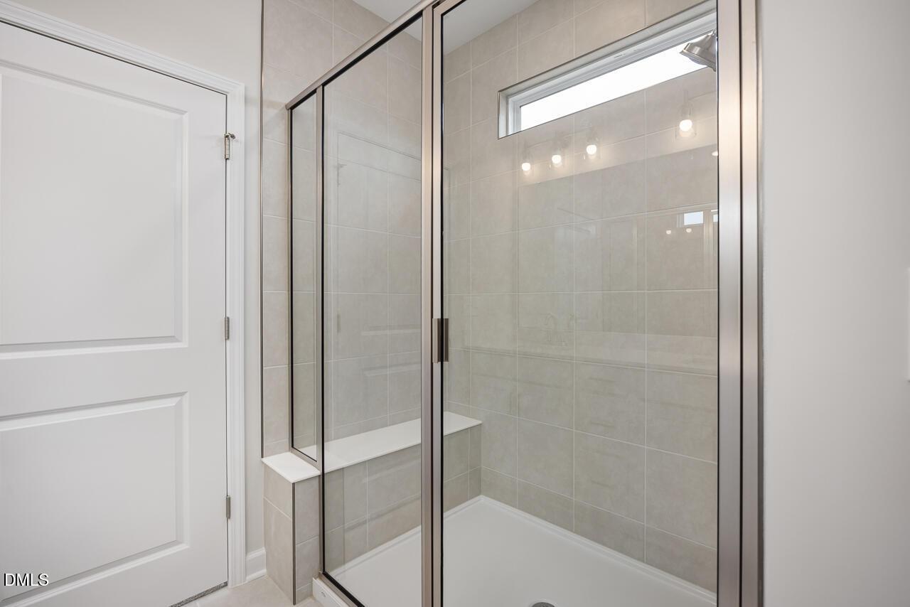 Frameless glass shower with tiled walls, bench seat, and frosted window in master bathroom of The Daphne C by Davidson Homes, Lillington, NC
