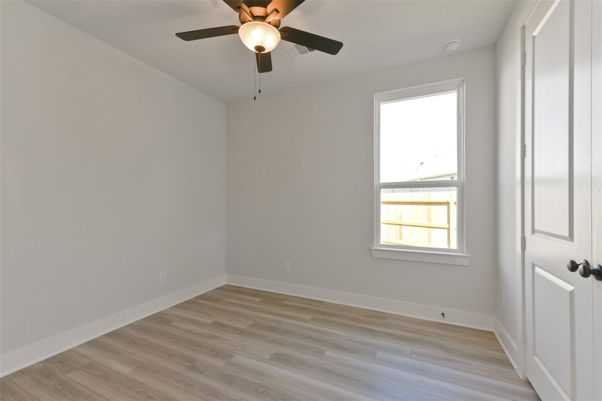 Bright secondary bedroom with ceiling fan, large window, double-door closet, neutral walls, and hardwood floors in Davidson Homes The Edward C, Lago Mar, Texas City