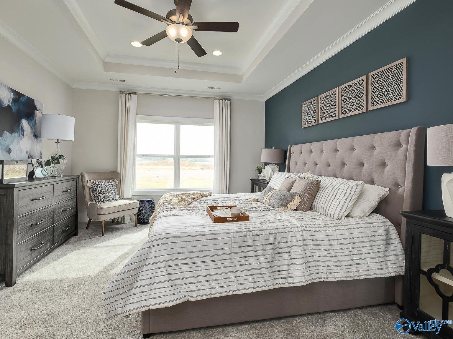 Serene master bedroom with tufted beige headboard, striped duvet, ceiling fan, and accent wall art in Davidson Homes The Everett, Toney, Alabama