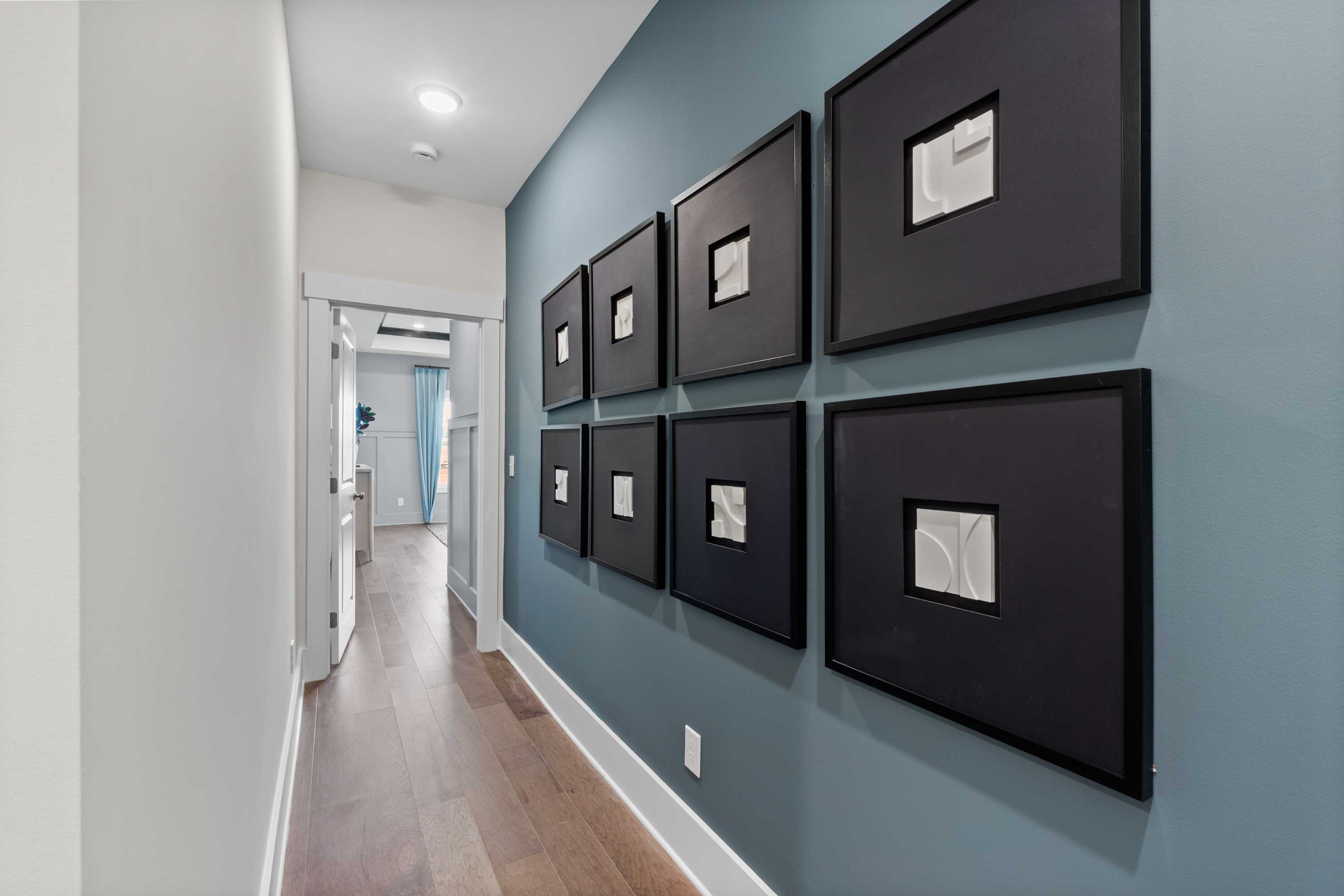 Elegant hallway in Creekside Harvest AL home with blue accent wall, six black-framed artworks, hardwood floors