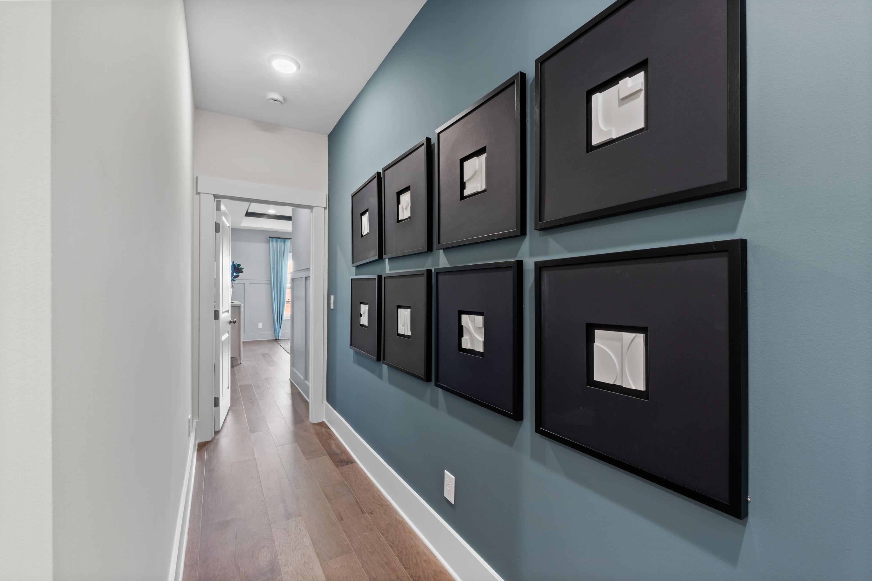 Elegant hallway in Creekside Harvest AL home with blue accent wall, six black-framed artworks, hardwood floors