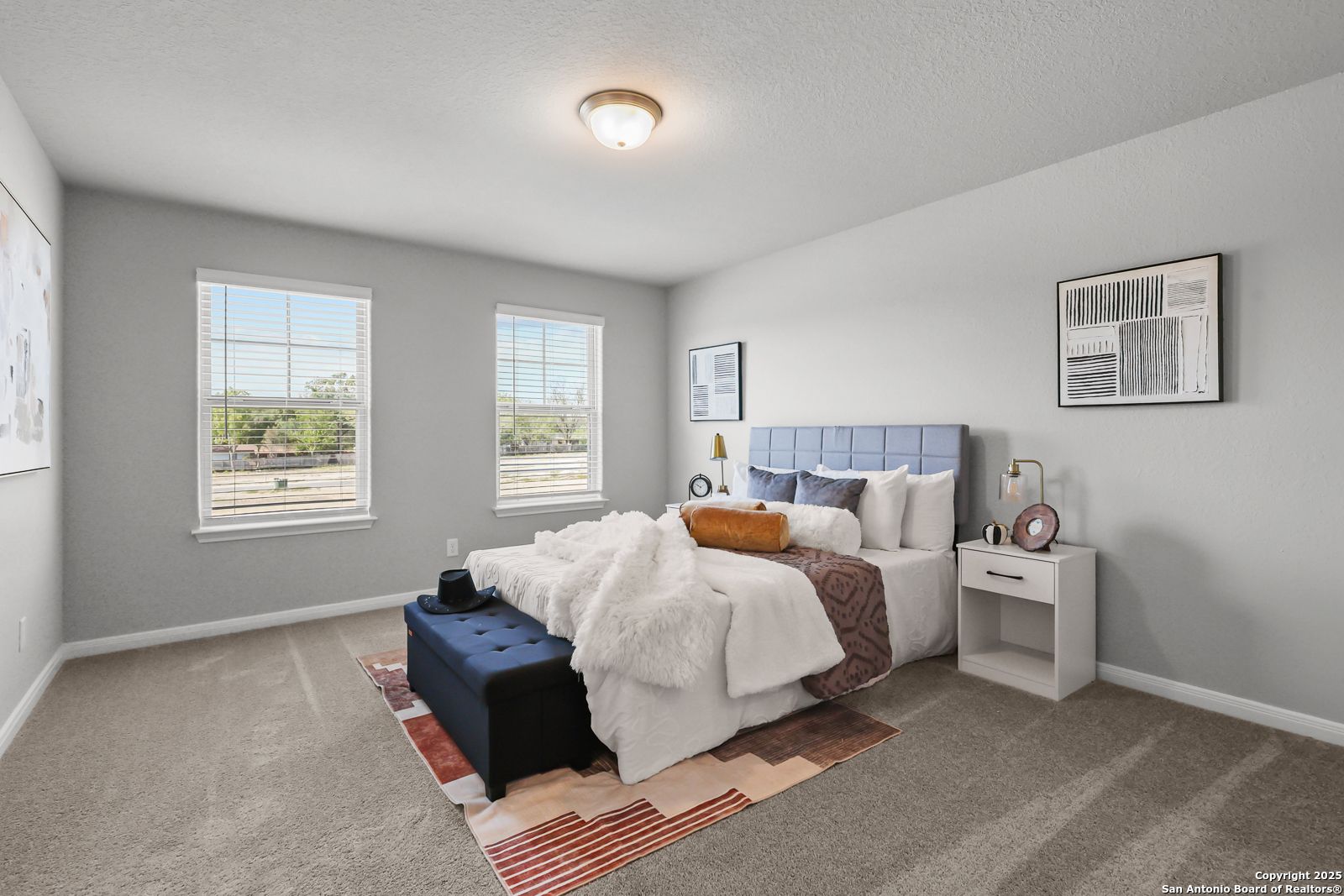 Cozy bedroom with tufted blue headboard bed, white duvet, bedside lamps, and large windows in Davidson Homes The Gillian C, San Antonio