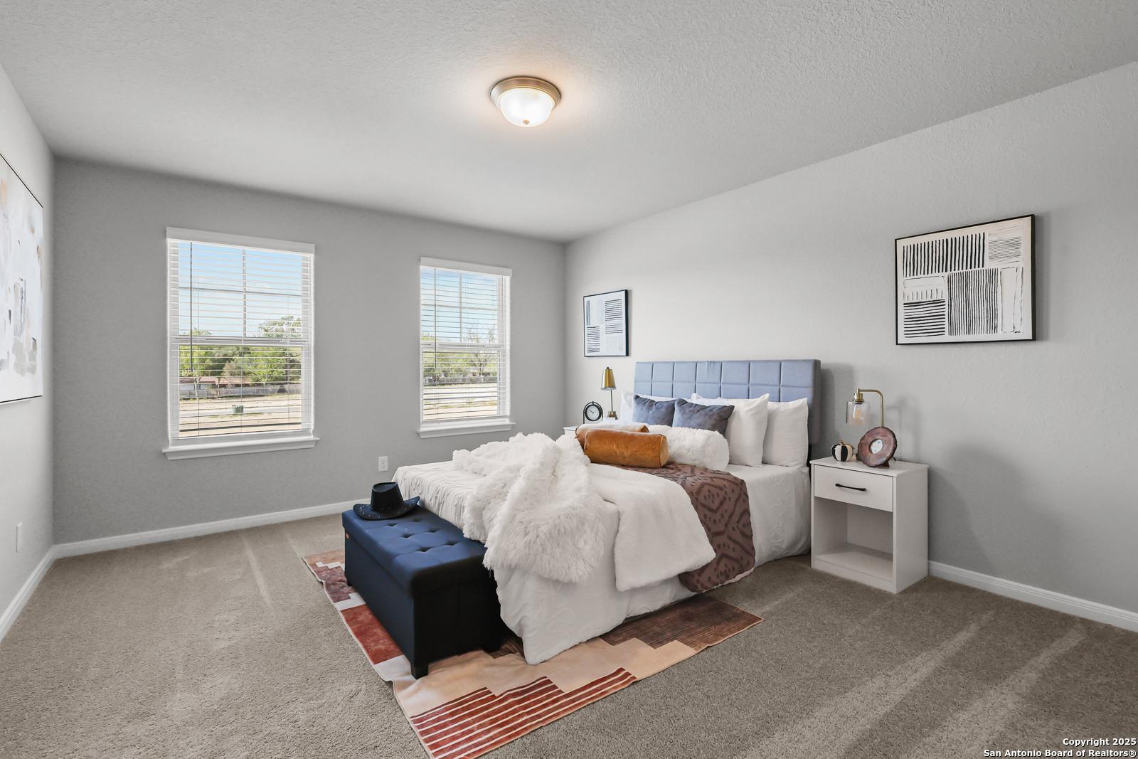 Cozy bedroom with tufted blue headboard bed, white duvet, bedside lamps, and large windows in Davidson Homes The Gillian C, San Antonio