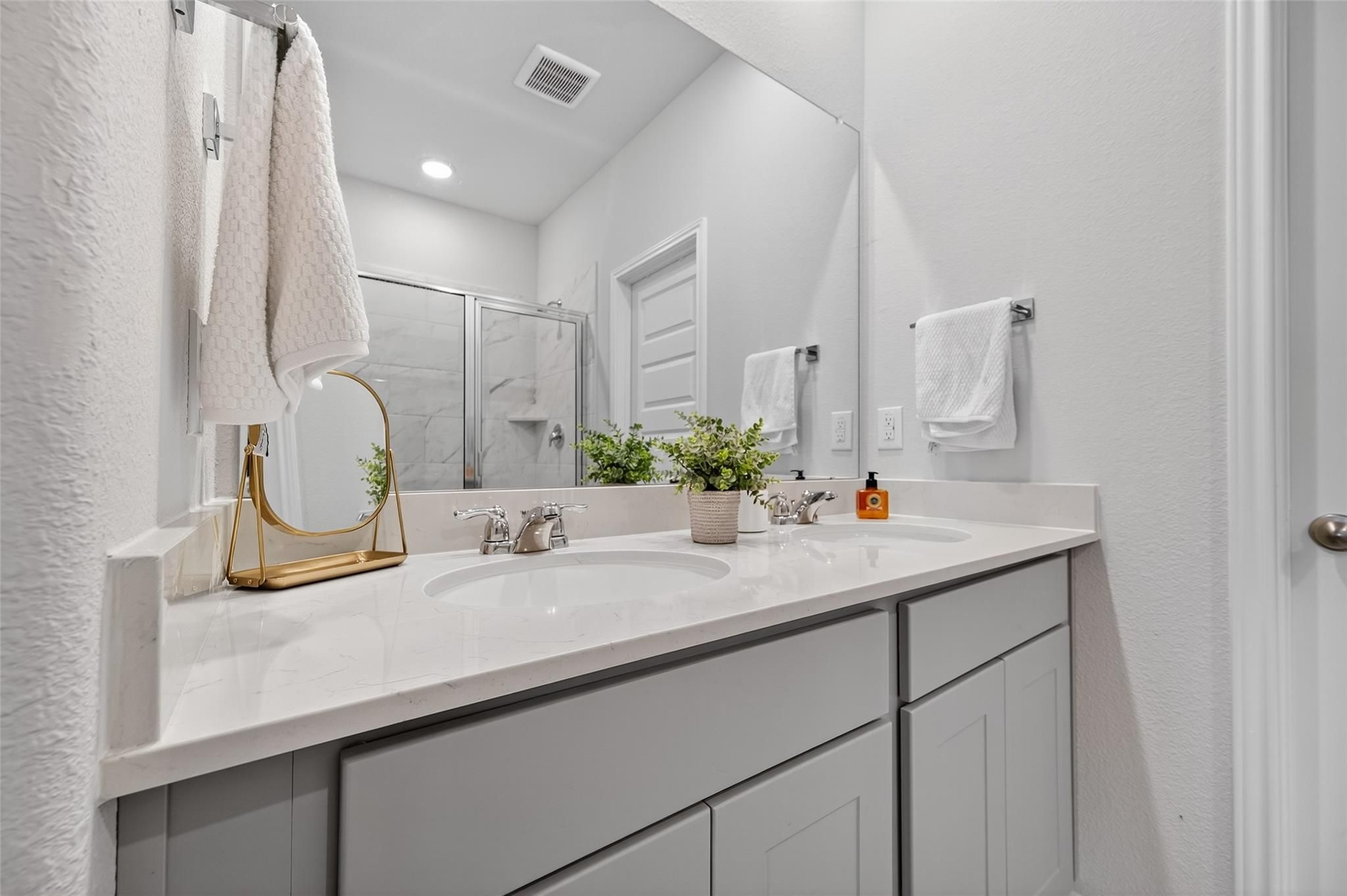 Elegant primary bathroom with dual quartz vanities, gray cabinets, and glass shower in Davidson Homes The Brazos E, Magnolia Texas
