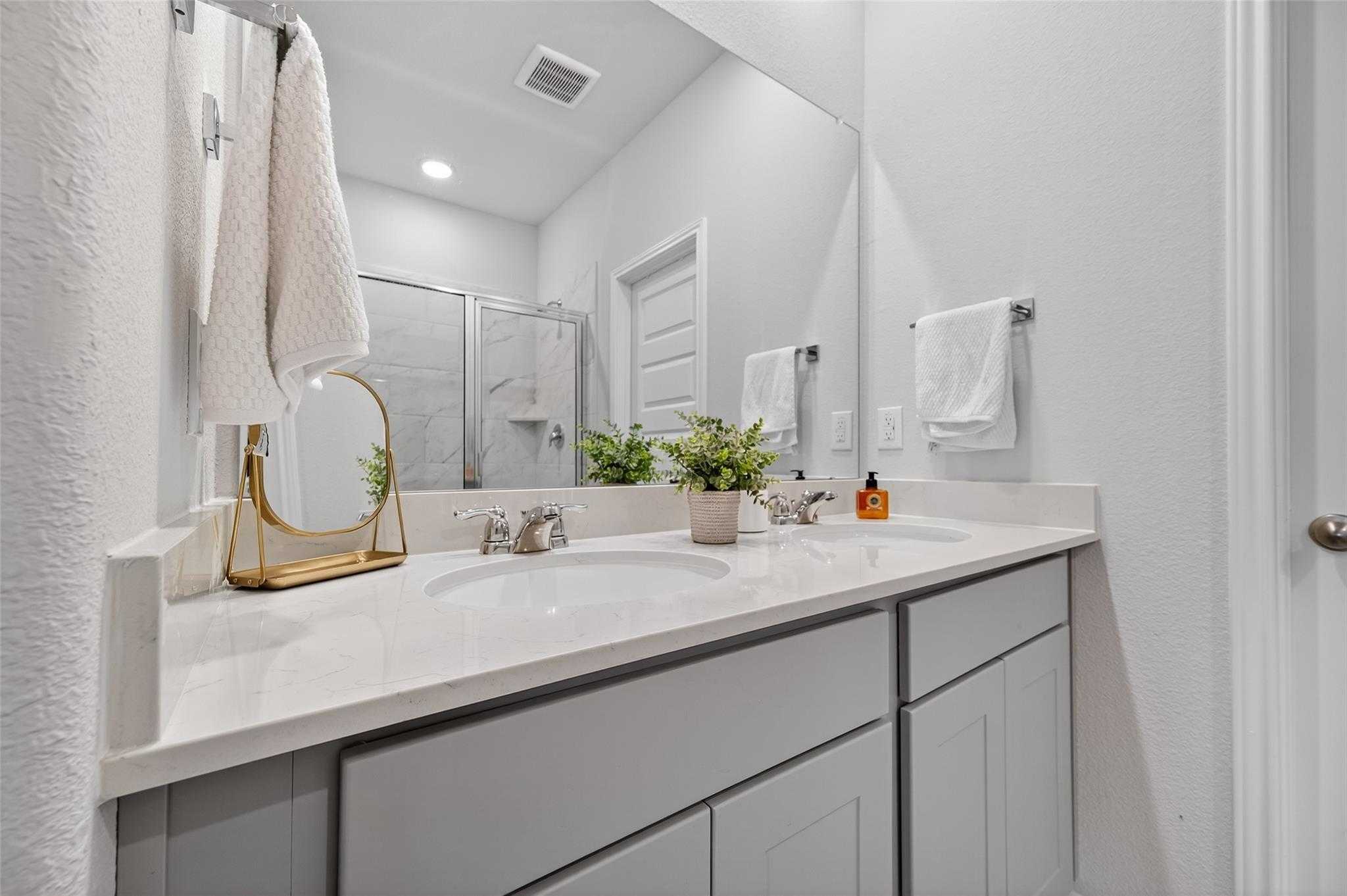 Elegant primary bathroom with dual quartz vanities, gray cabinets, and glass shower in Davidson Homes The Brazos E, Magnolia Texas
