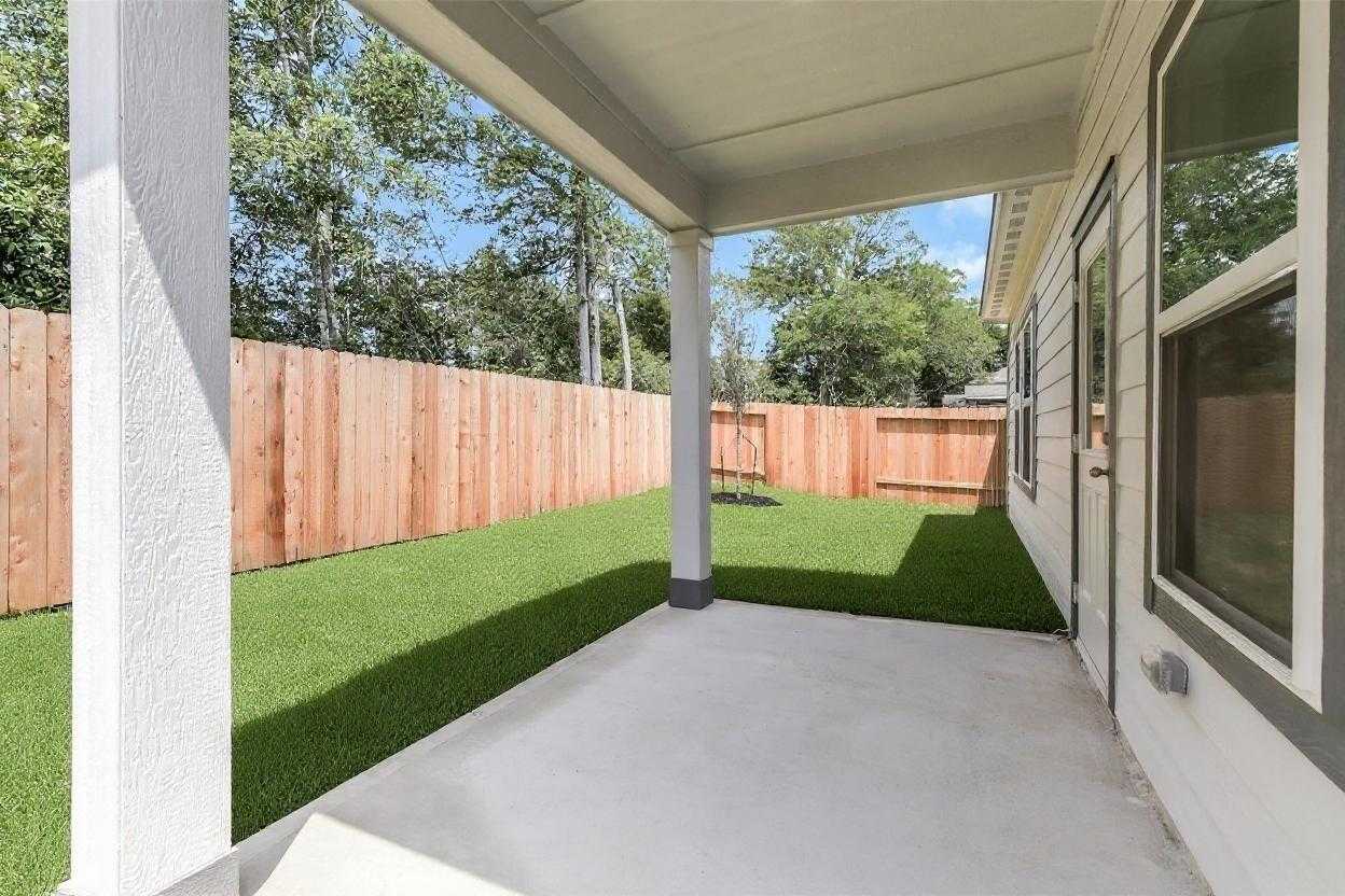 Covered patio with lush green lawn, wooden fence, trees, and swing set in backyard of Davidson Homes The Sabine E, Conroe, Texas