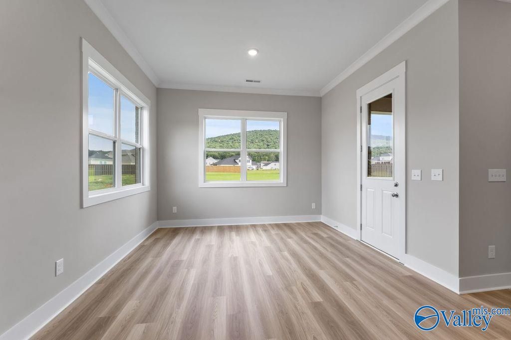 Bright empty room with large windows overlooking green landscape, hardwood floors in Evermore Homes The Oxford, Owens Cross Roads, AL