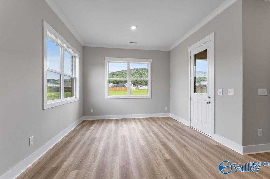 Bright empty room with large windows overlooking green landscape, hardwood floors in Evermore Homes The Oxford, Owens Cross Roads, AL