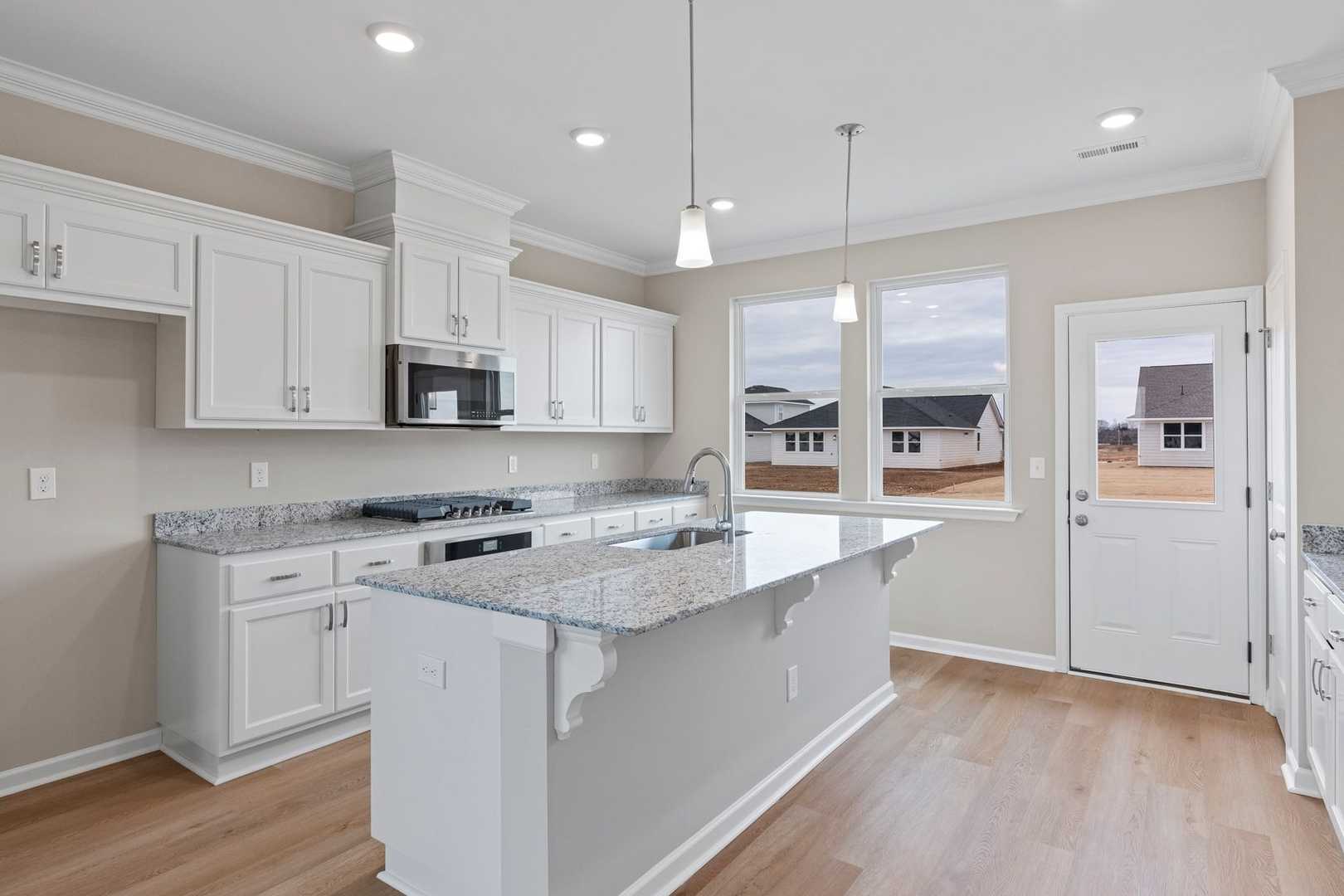 Bright kitchen in The Stella by Evermore Homes featuring white cabinets, granite island, stainless appliances, and backyard view