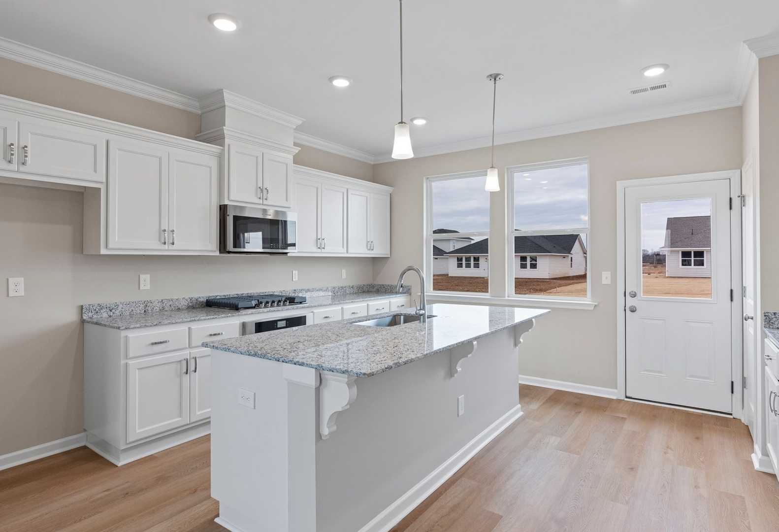 Spacious kitchen in The Stella A home featuring white shaker cabinets, granite island, and stainless appliances