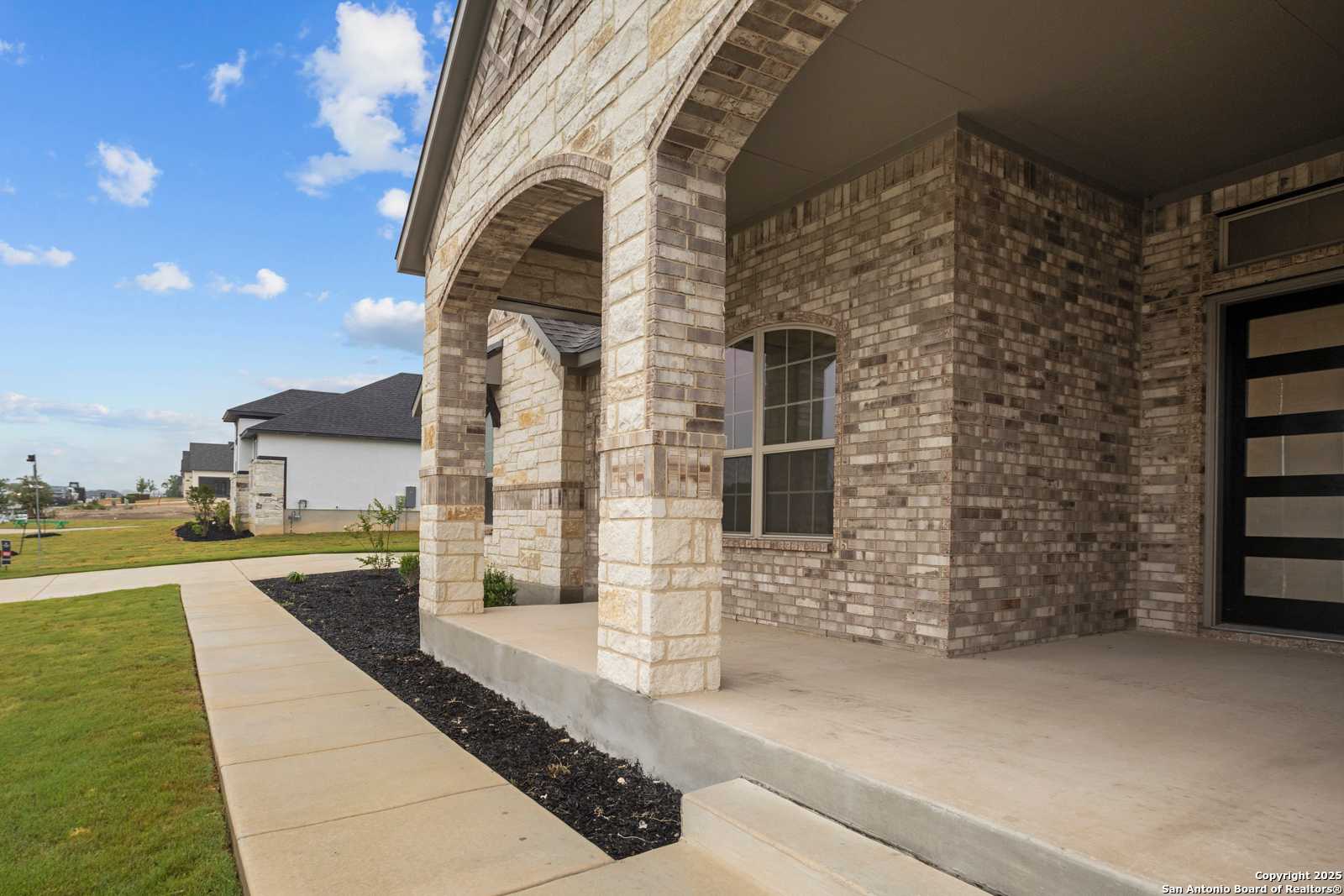 Modern stone and brick single-story home with arched porch, 3-car garage, and landscaped walkway in Potranco Oaks, Castroville, Texas