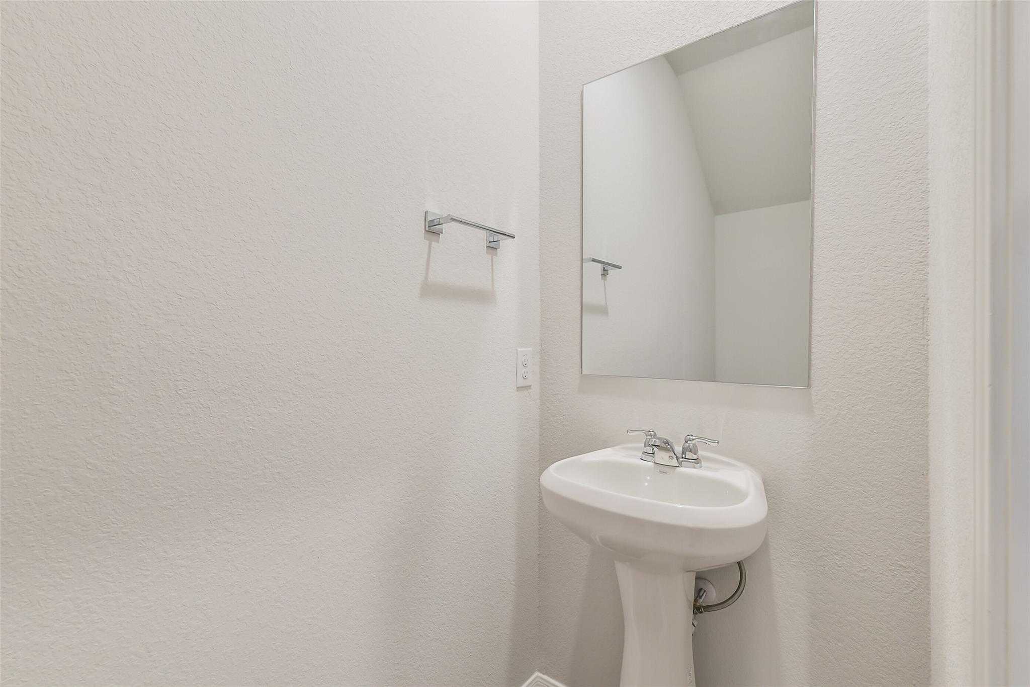 Elegant powder room featuring pedestal sink, frameless mirror, and white walls in Davidson Homes The Brazos F, Conroe, Texas