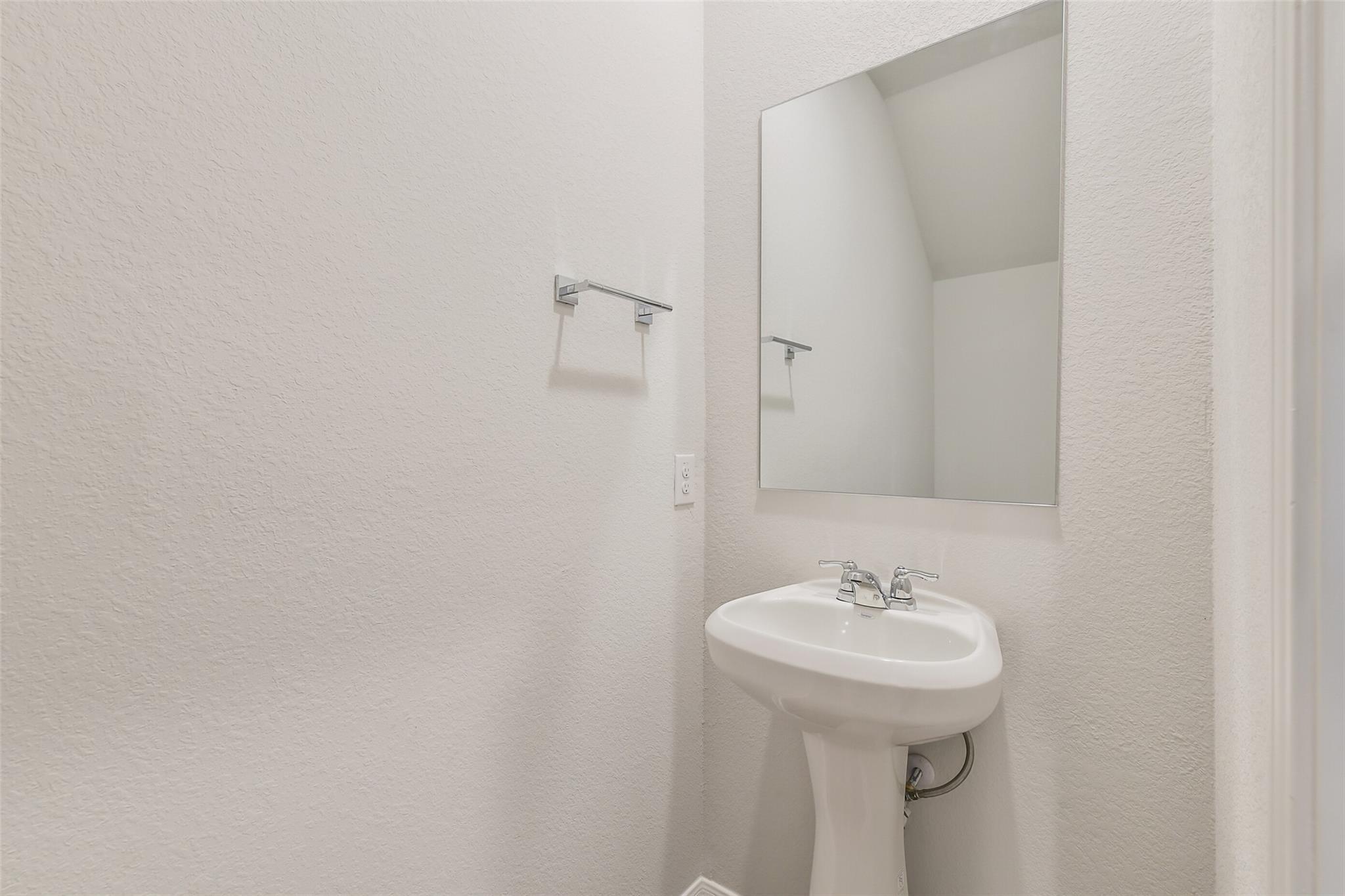 Elegant powder room with white pedestal sink, frameless mirror and towel bar in Davidson Homes The Brazos F, Conroe, Texas