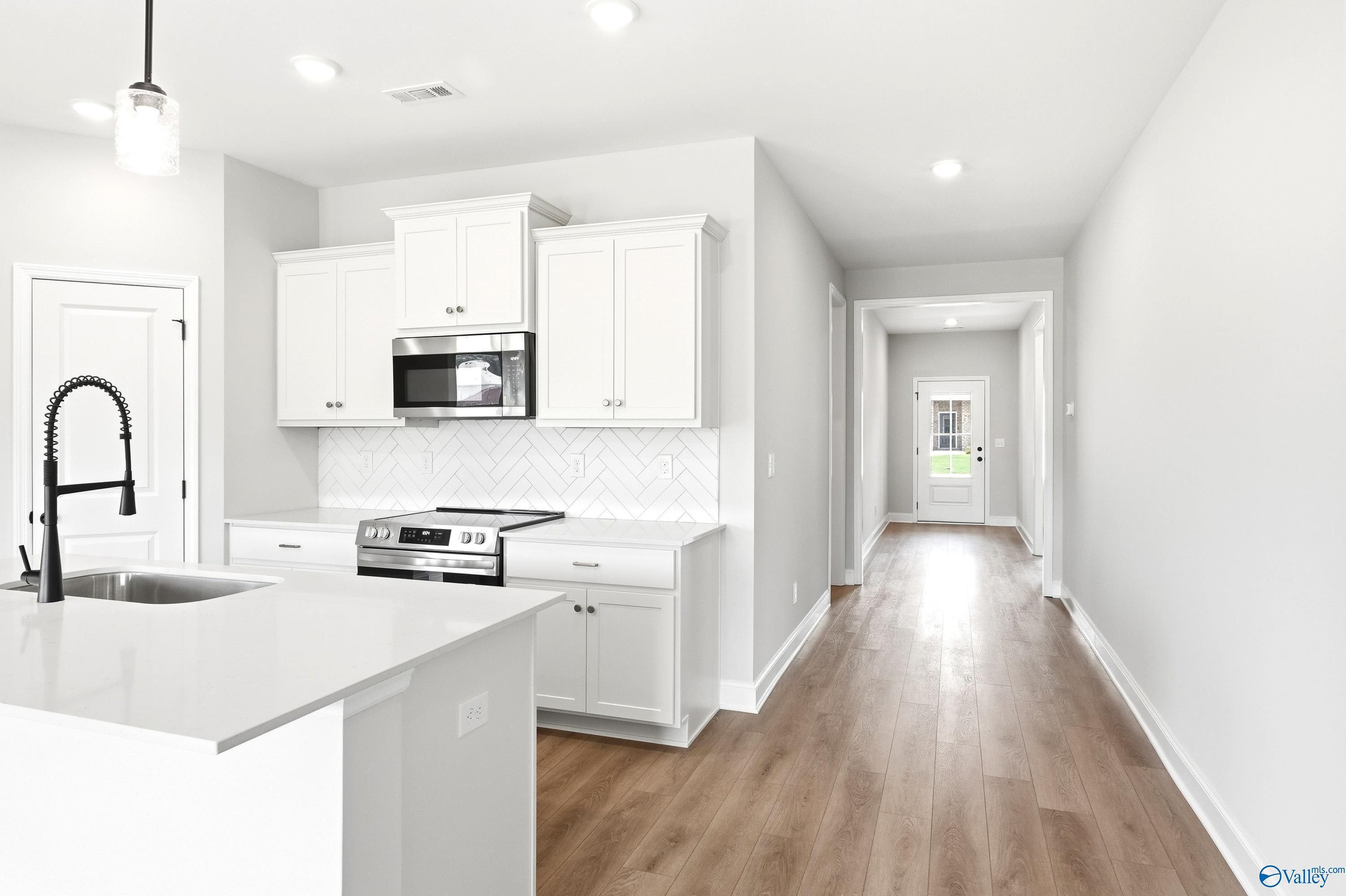 Modern kitchen with white cabinets, herringbone backsplash, and island in The Daphne floor plan at Lynn Meadows, Alabama.