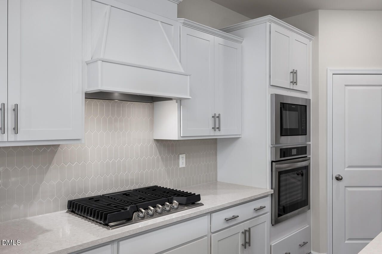 Contemporary kitchen with white shaker cabinets, herringbone tile backsplash, quartz counters, stainless gas range in The Grace C floor plan, Lillington, NC