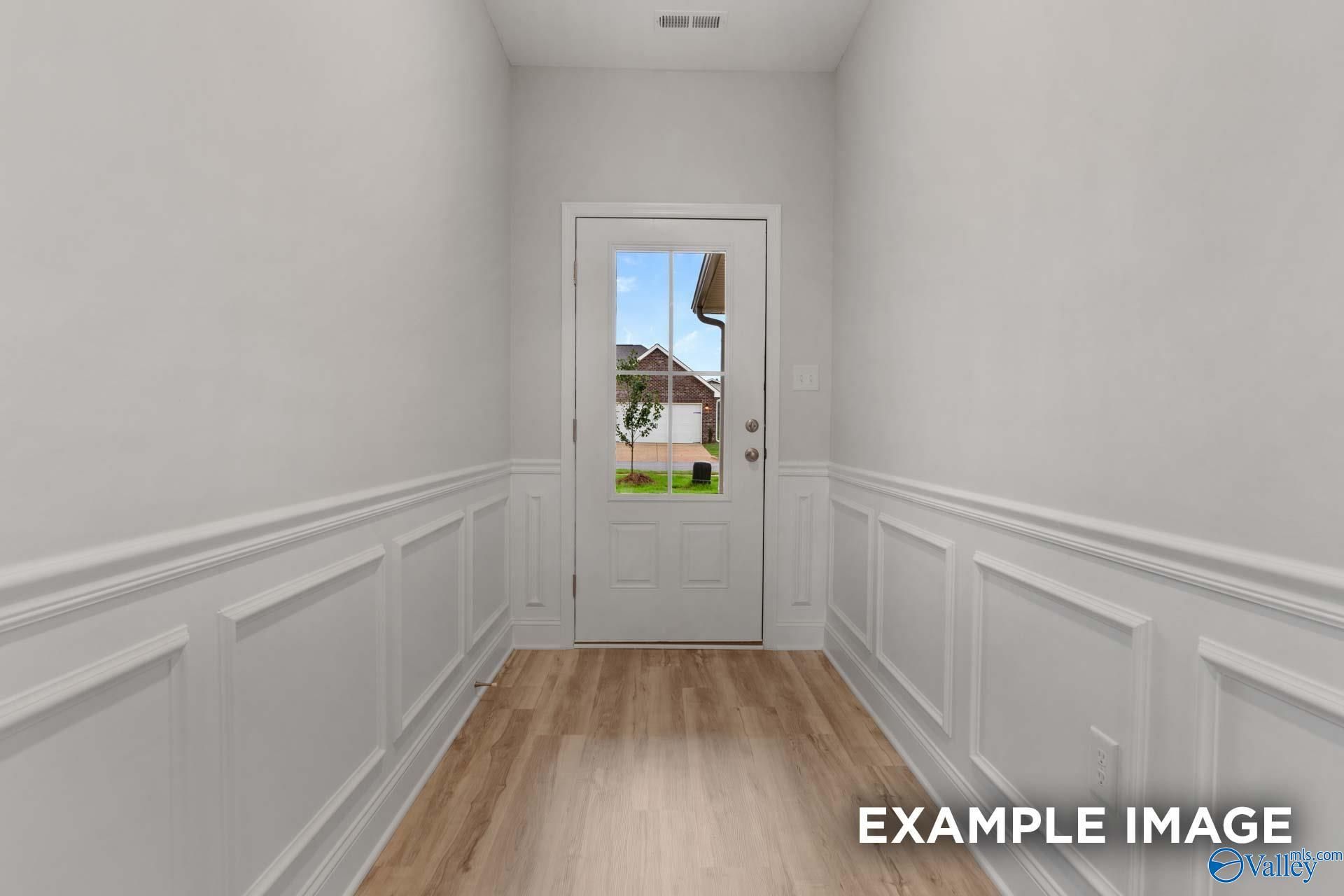 Bright hallway with white wainscoting, hardwood floors, and glass-paneled door to backyard in Davidson Homes The Cumberland B, Decatur, Alabama