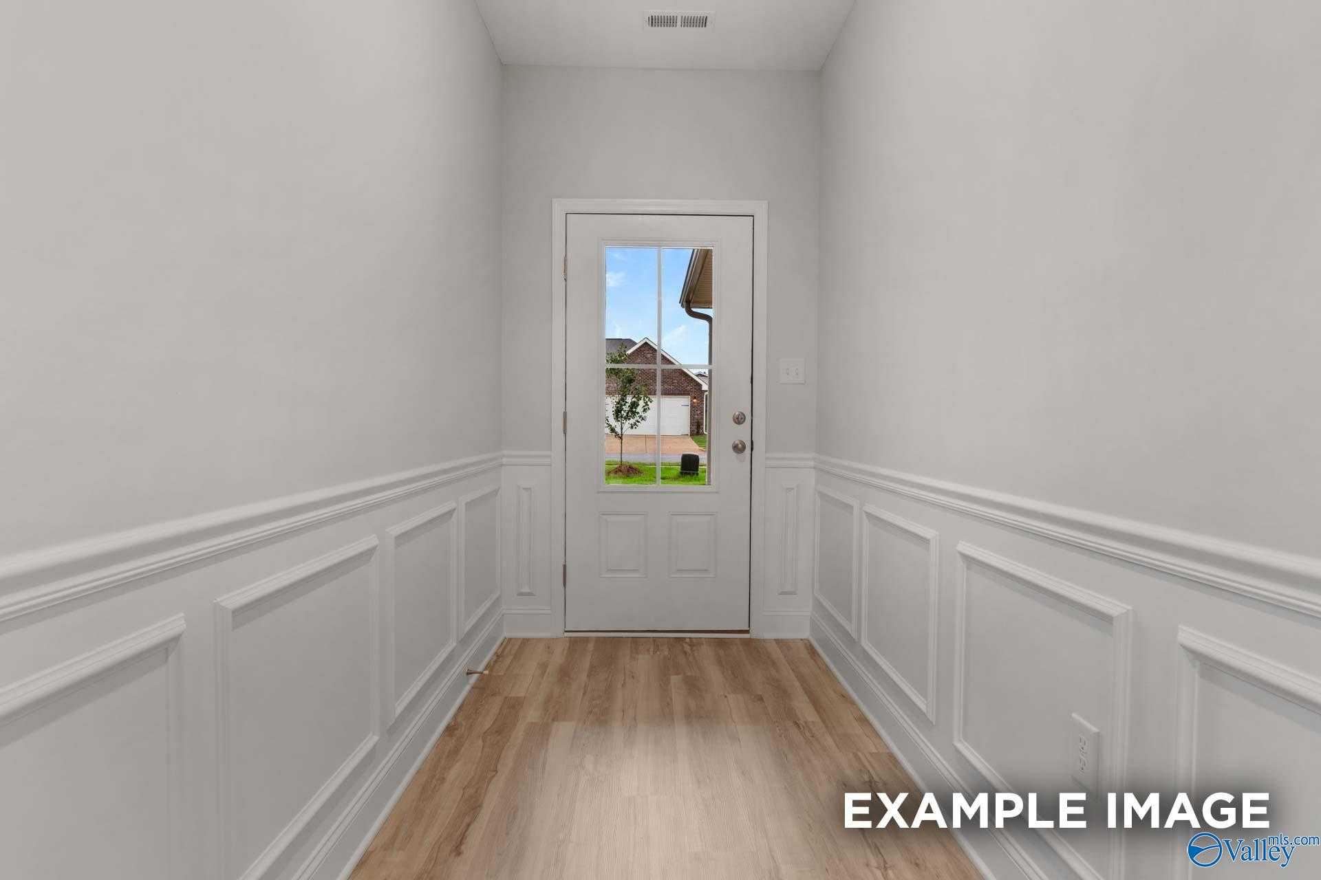 Bright hallway with white wainscoting, hardwood floors, and glass-paneled door to backyard in Davidson Homes The Cumberland B, Decatur, Alabama