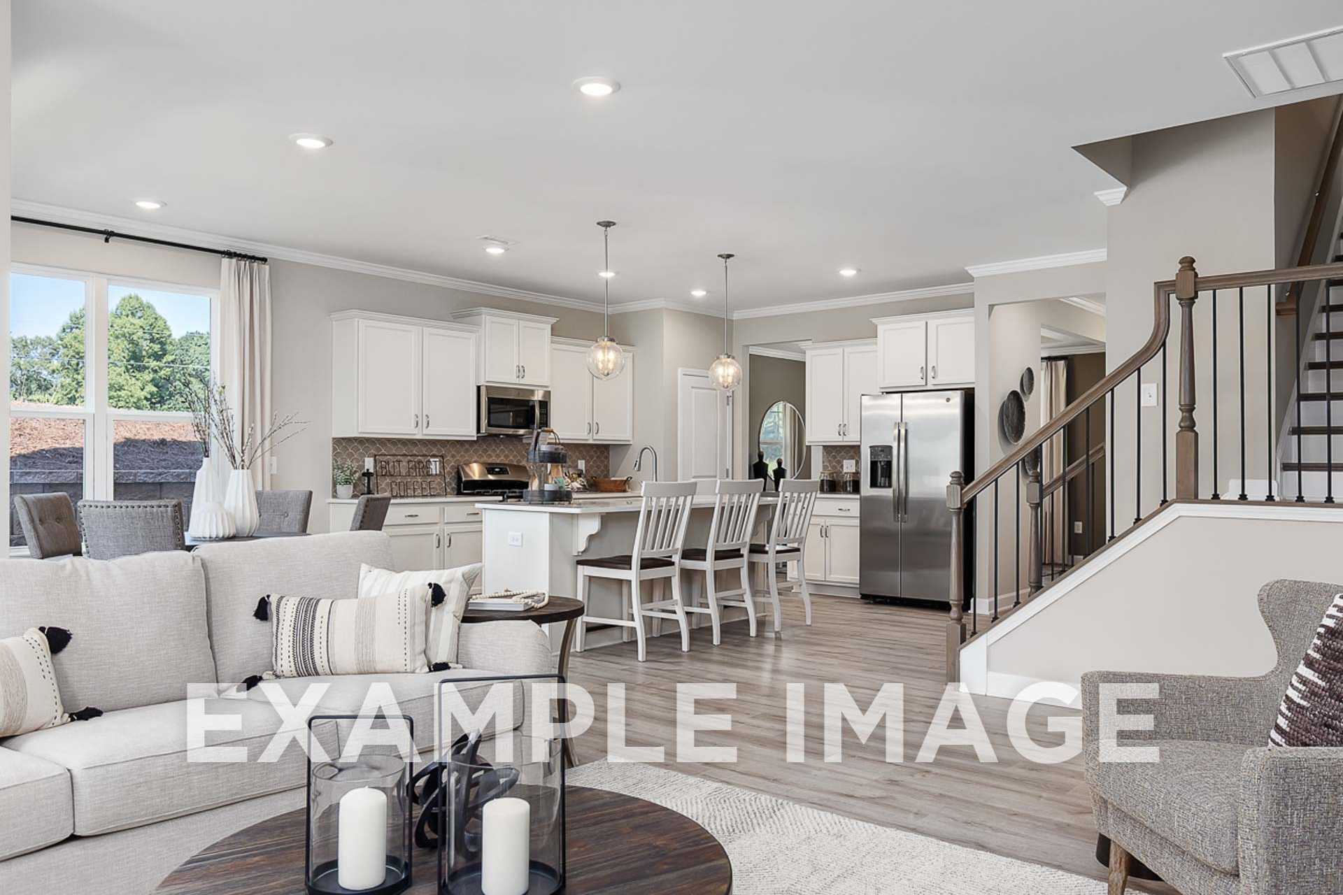 Spacious open-concept kitchen and living area in The Ash E home design, white cabinets, large island, stainless appliances, hardwood floors