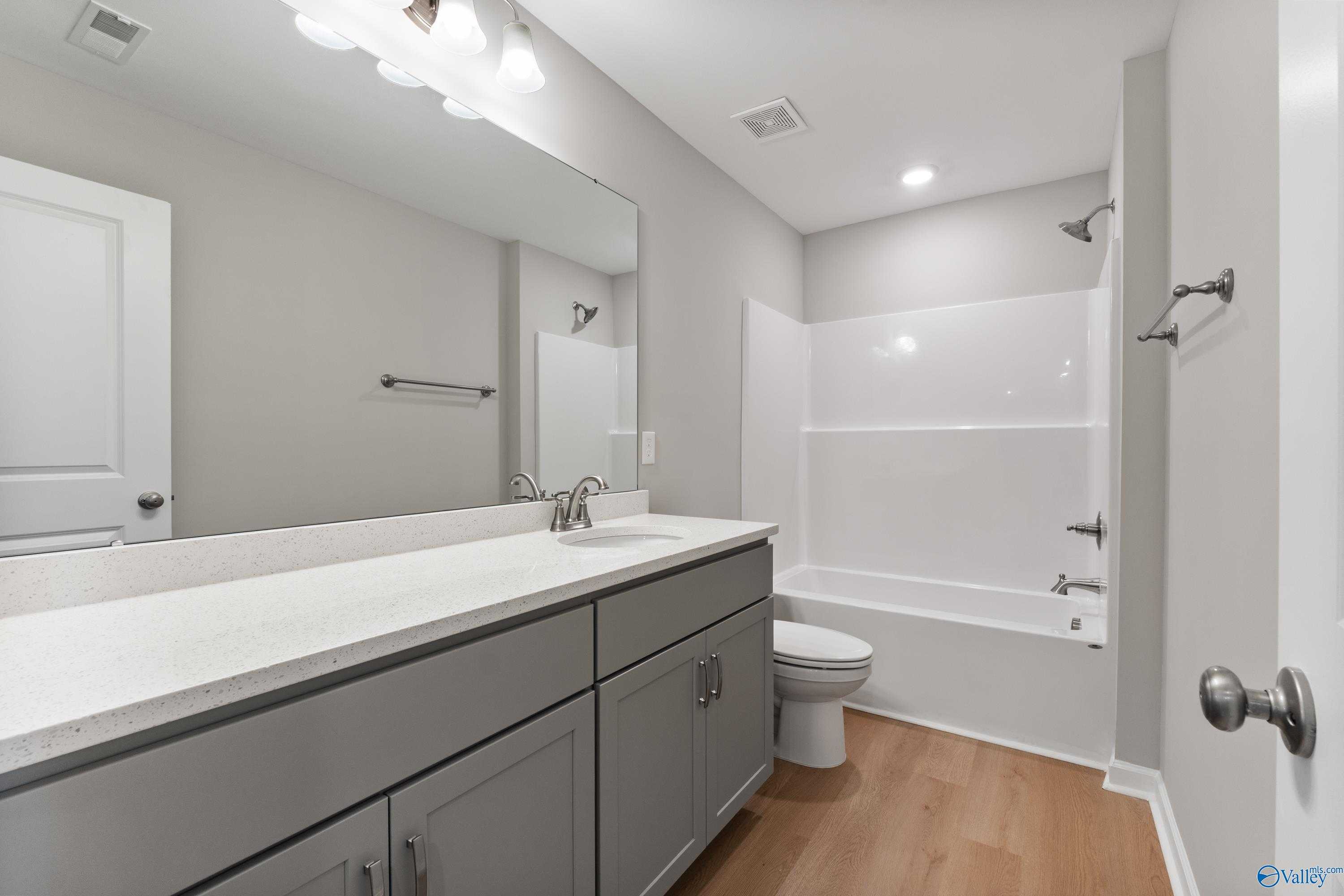 Contemporary bathroom with gray vanity, white tub, shower, and large mirror in Davidson Homes The Charm, Huntsville, AL