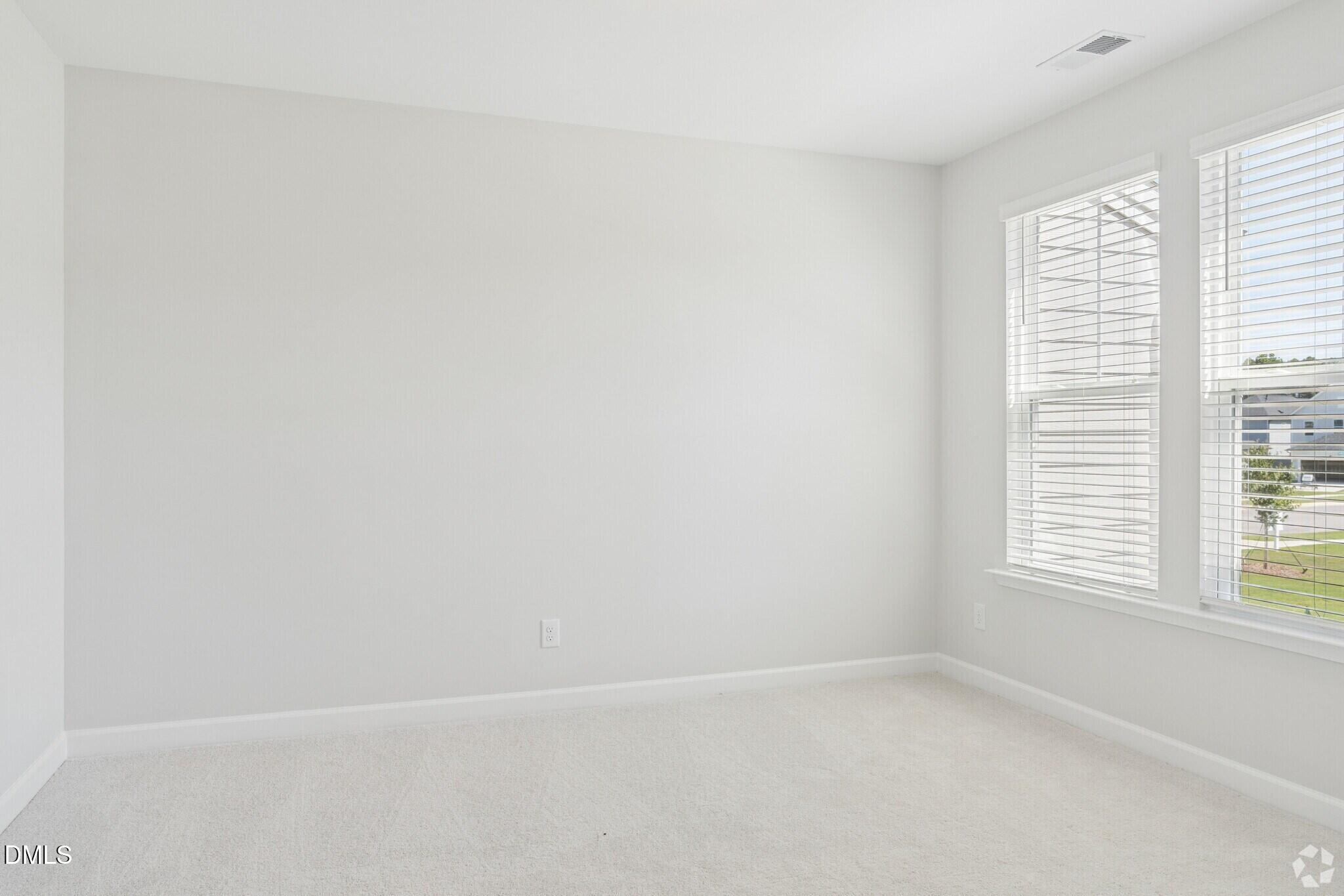 Bright empty bedroom with white carpet, neutral walls, and double windows with blinds in Davidson Homes' The Mitchell, Knightdale NC