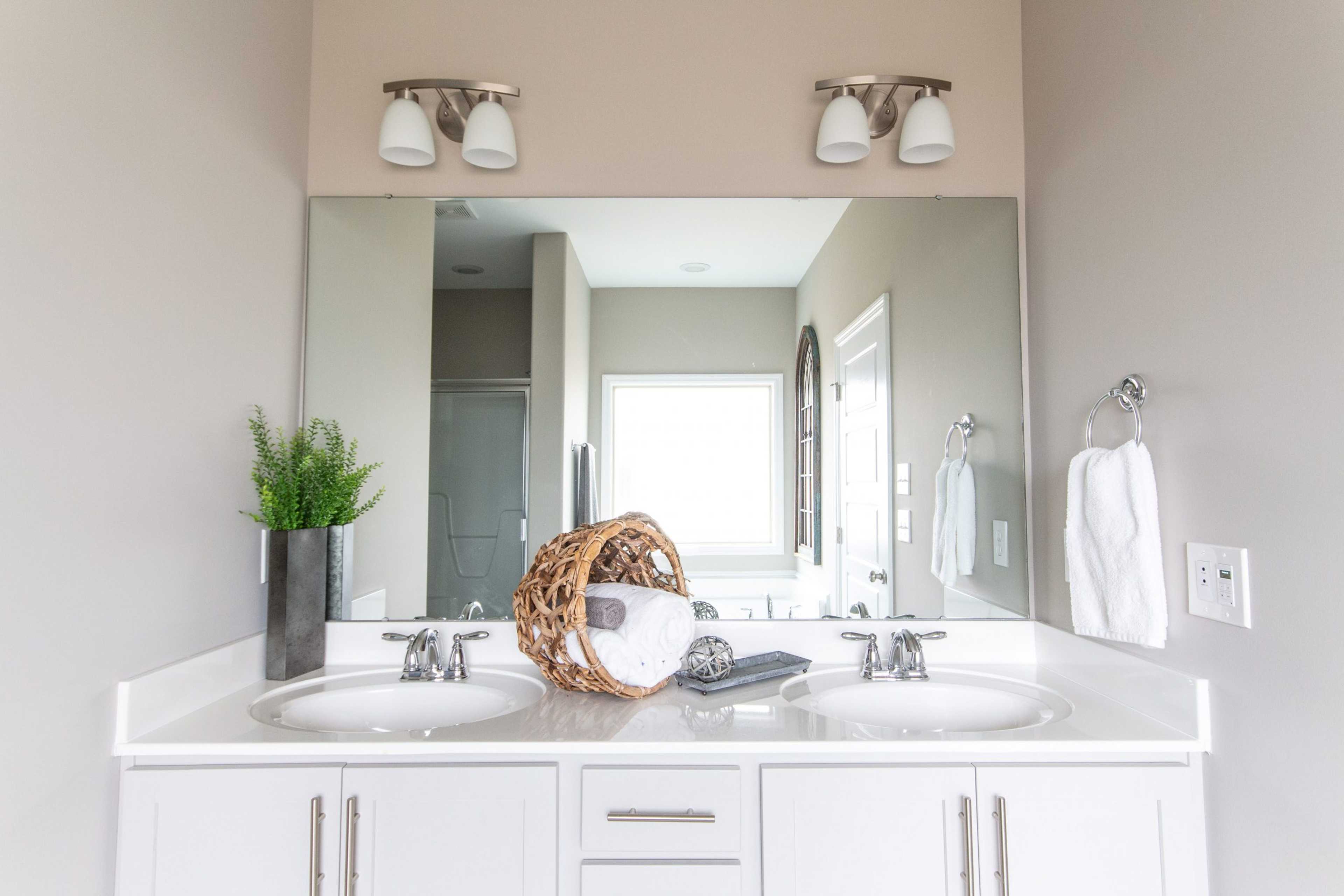 Elegant double vanity bathroom at Bakers Farm in Priceville, Alabama with framed mirror, sconce lights, and potted fern