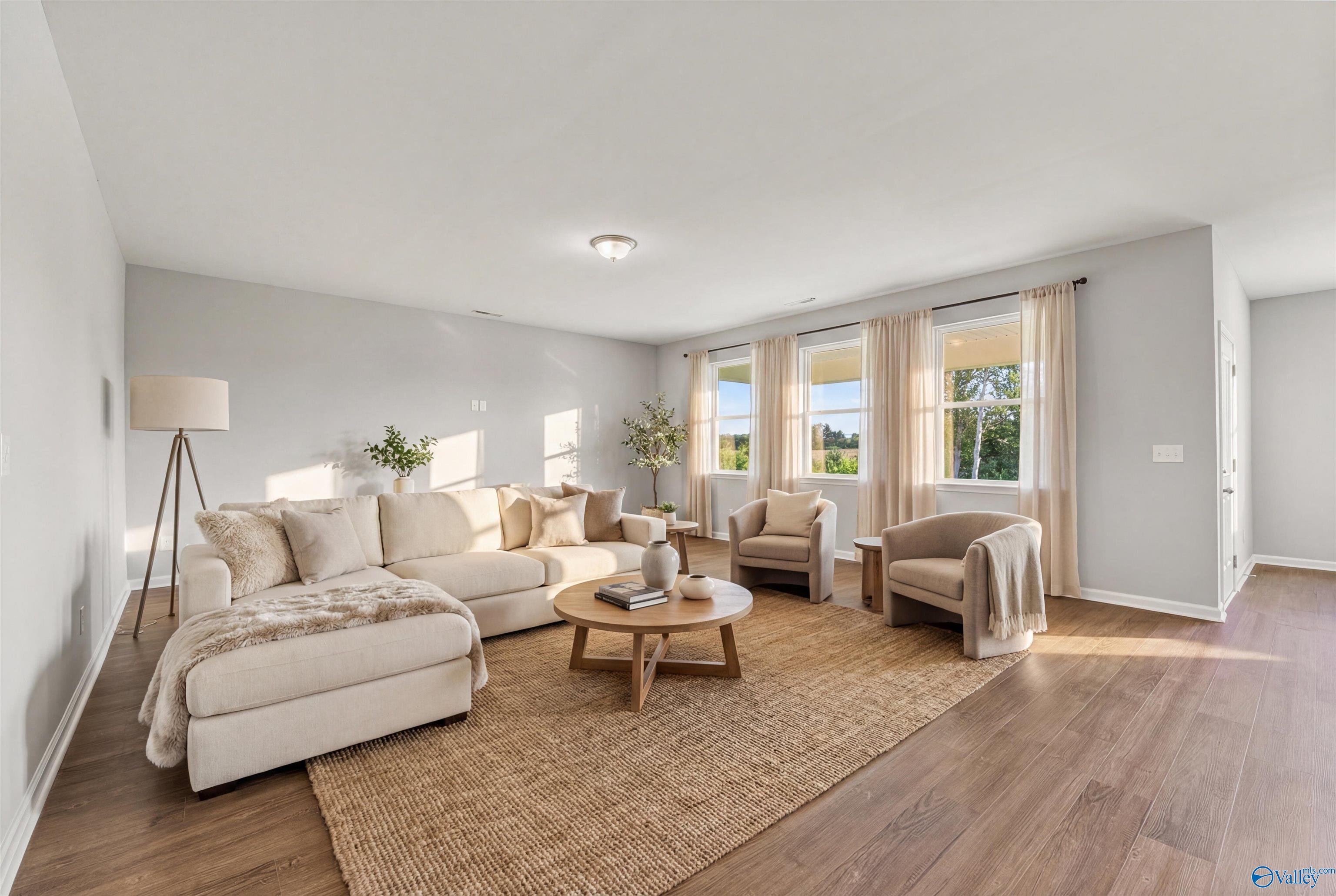 Cozy living room with beige sectional sofa, wooden coffee table, armchairs, seagrass rug on hardwood floors in Davidson Homes The Sanctuary, Huntsville