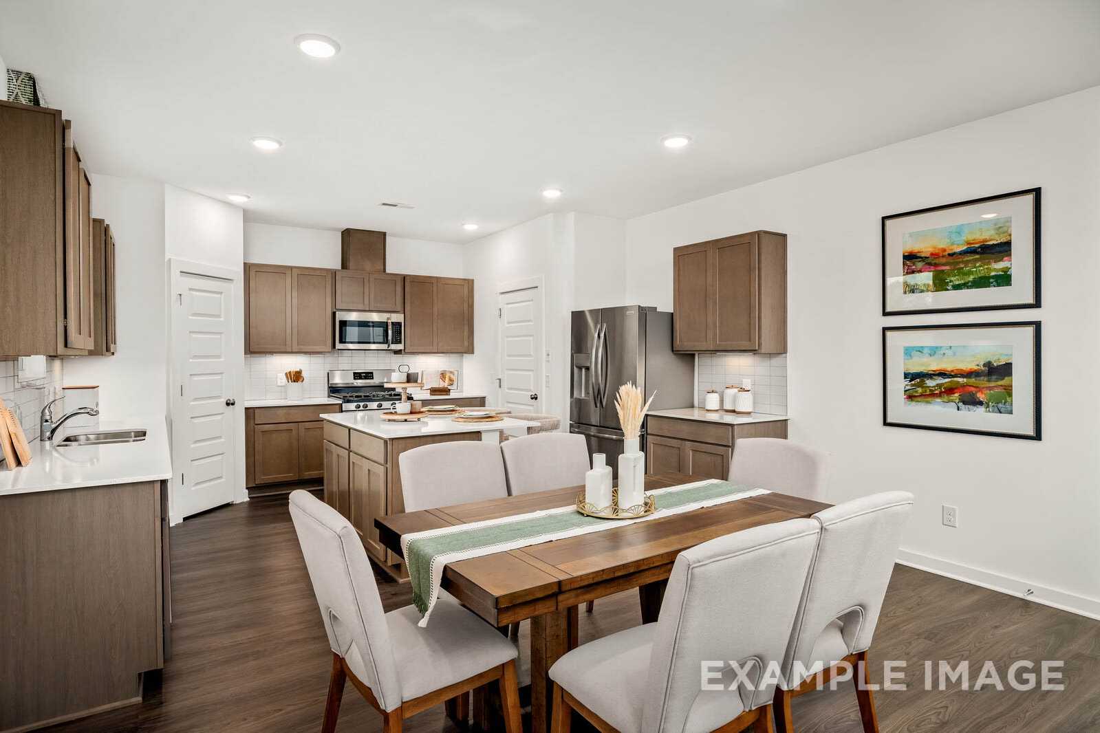 Spacious open-concept kitchen and dining in The Gordon B, featuring brown shaker cabinets, stainless appliances, island, and wooden table
