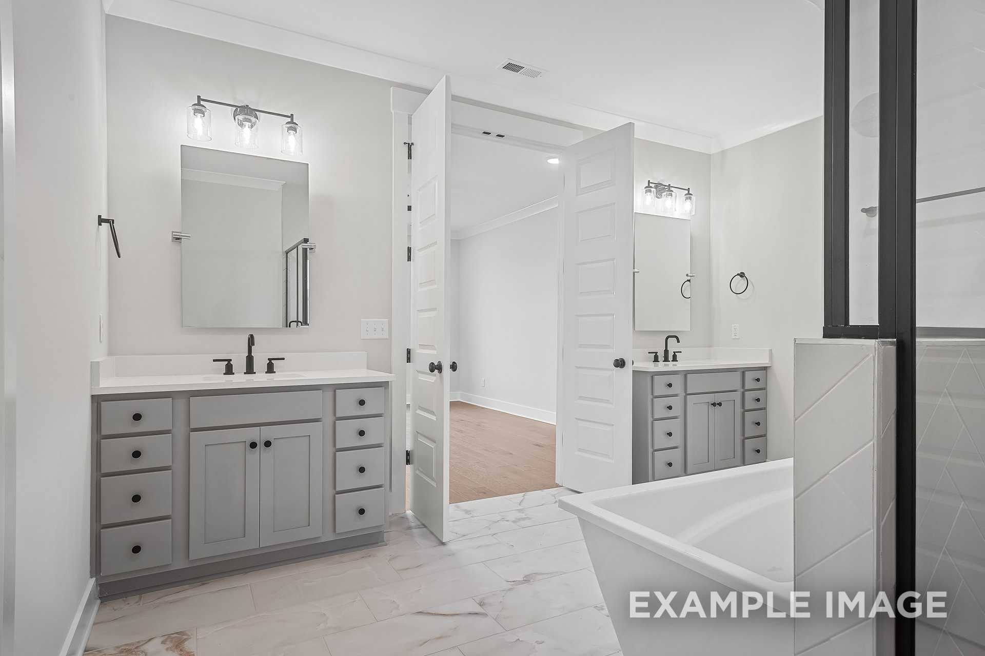 Spacious master bathroom in The Hathaway with dual gray vanities, freestanding soaking tub, and open tiled layout