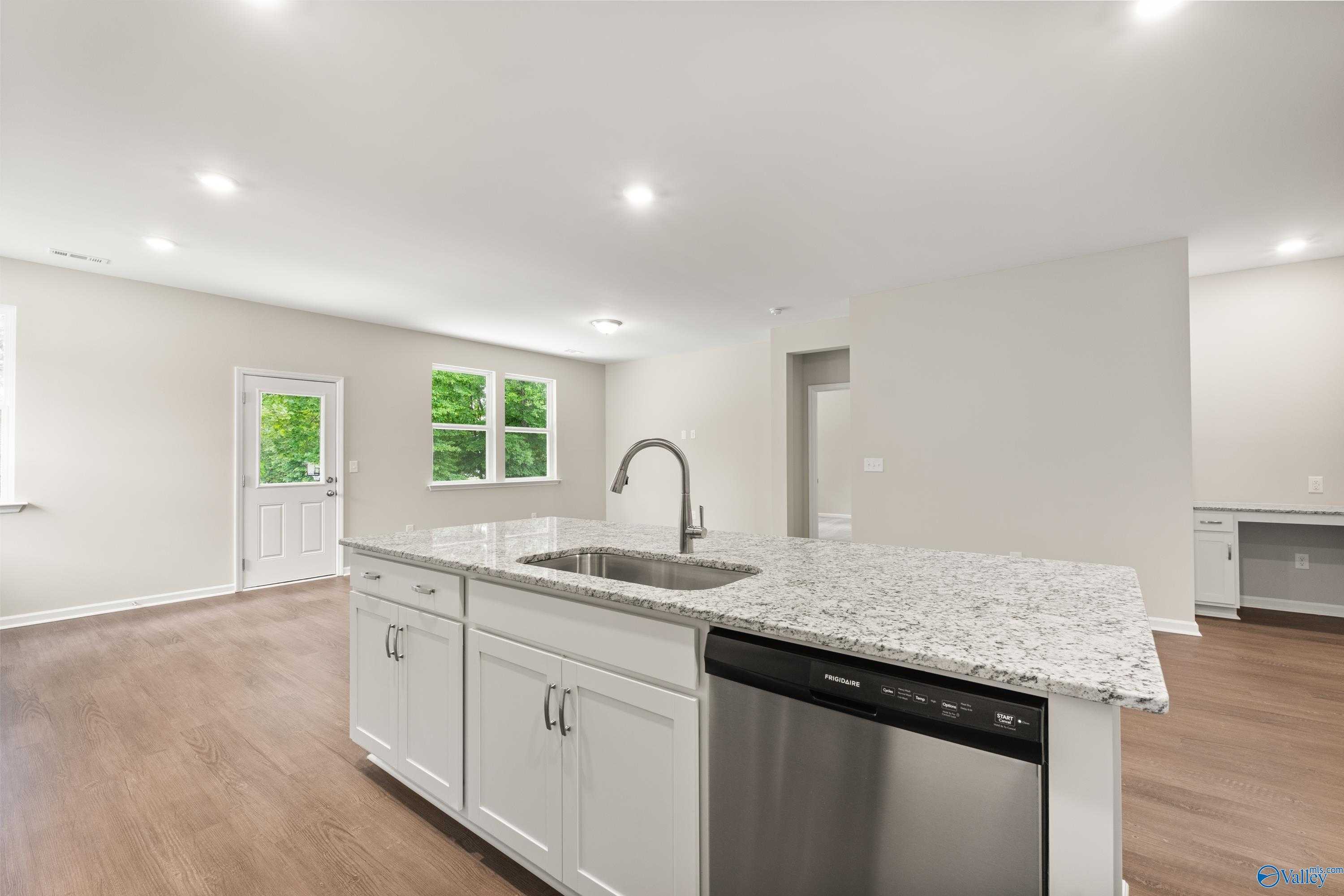 Bright open-concept kitchen with white cabinets, granite island sink, stainless dishwasher in Davidson Homes The Phoenix, Fayetteville TN