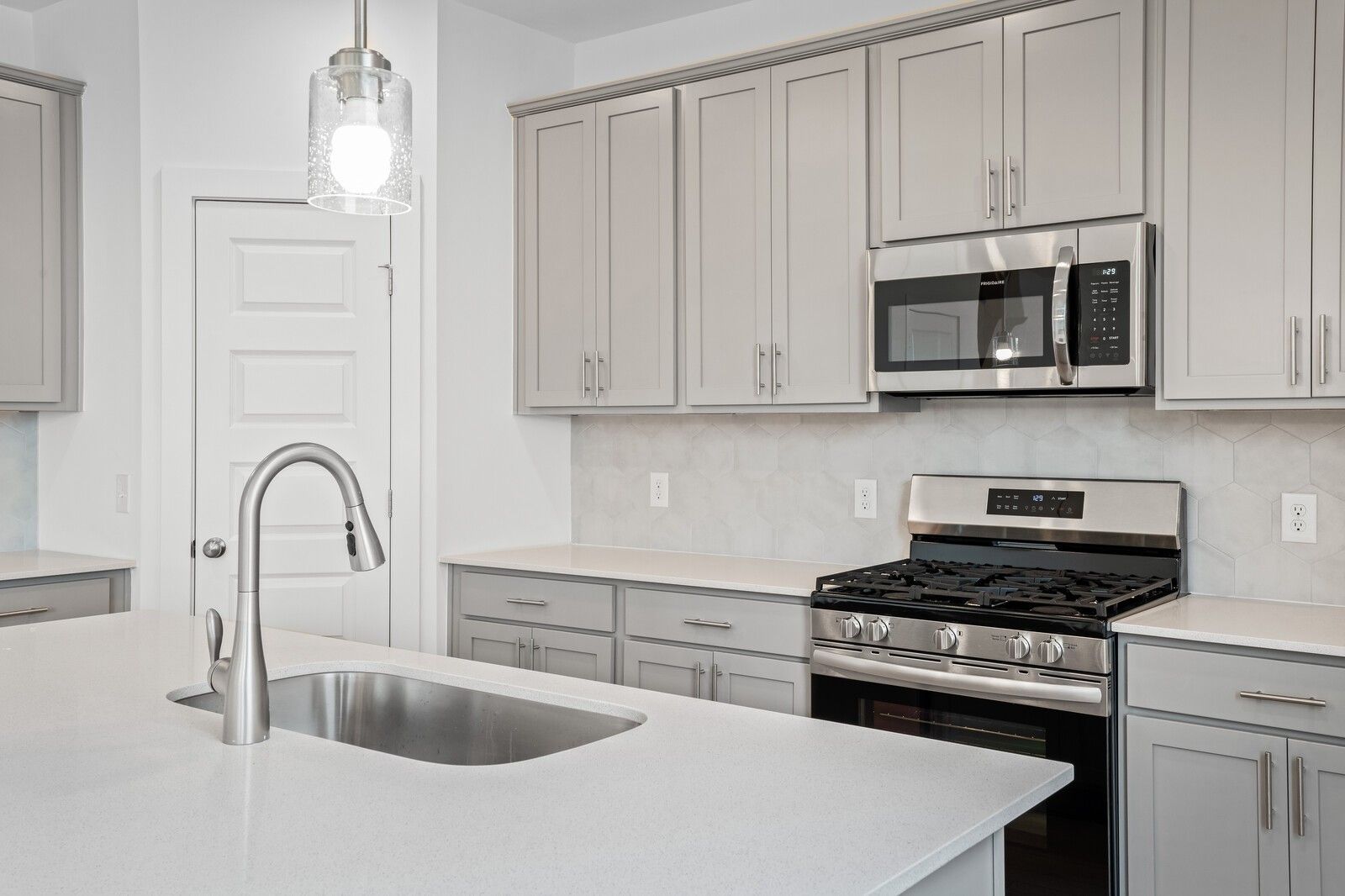 Modern kitchen with gray cabinets, quartz countertops, and stainless appliances in The Logan C plan at Calista Farms.
