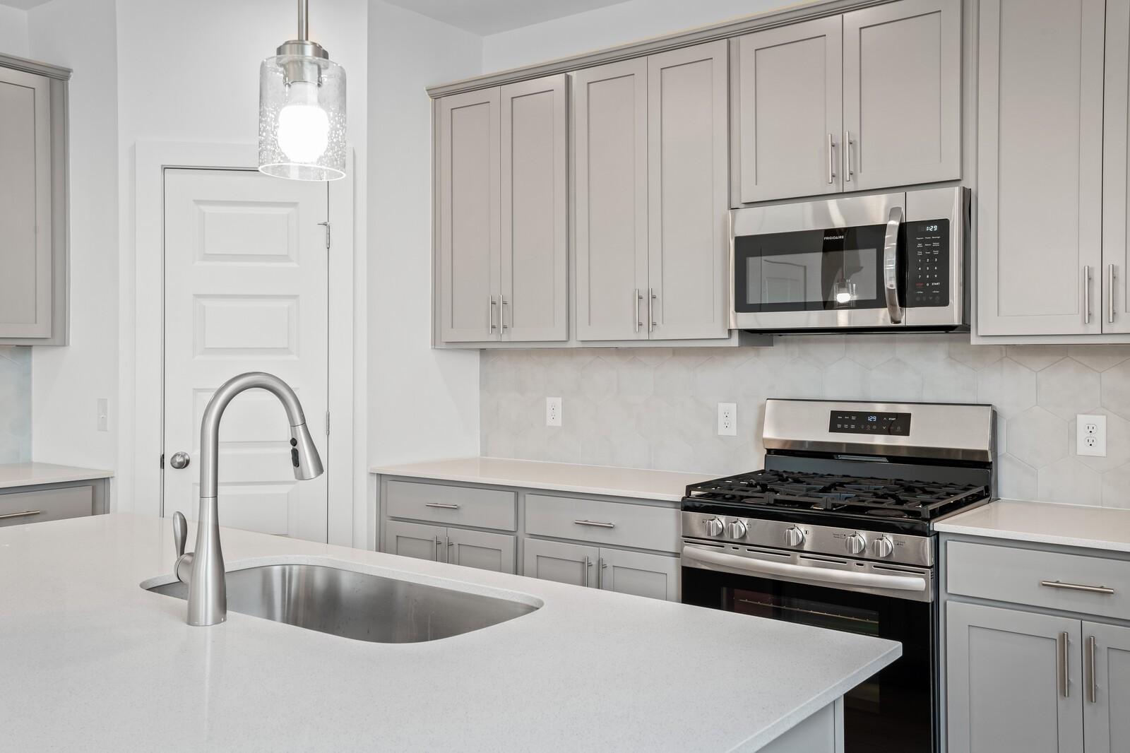 Modern kitchen with gray cabinets, quartz countertops, and stainless appliances in The Logan C plan at Calista Farms.