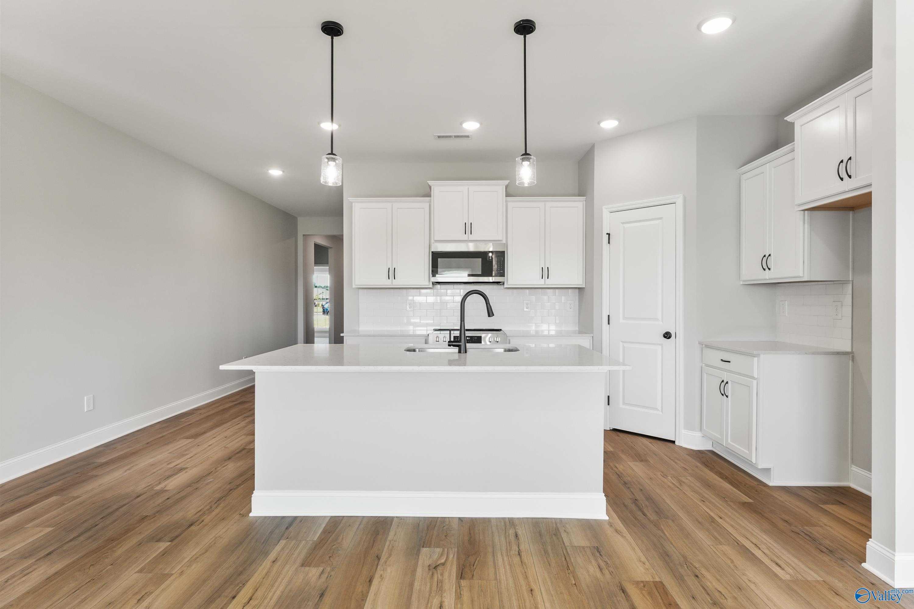 Modern white kitchen island with pendant lights, hardwood floors, and open layout in The Daphne C 4-bedroom home by Davidson Homes, Hazel Green, Alabama