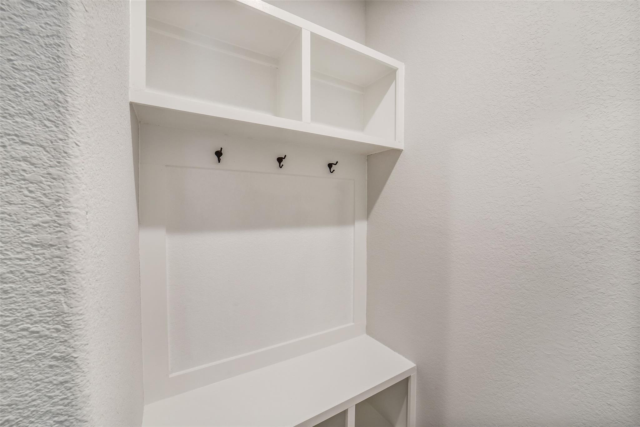 White built-in mudroom cabinet with open shelves, coat hooks, bench, and cubbies in Davidson Homes The Acadia C, Magnolia Texas