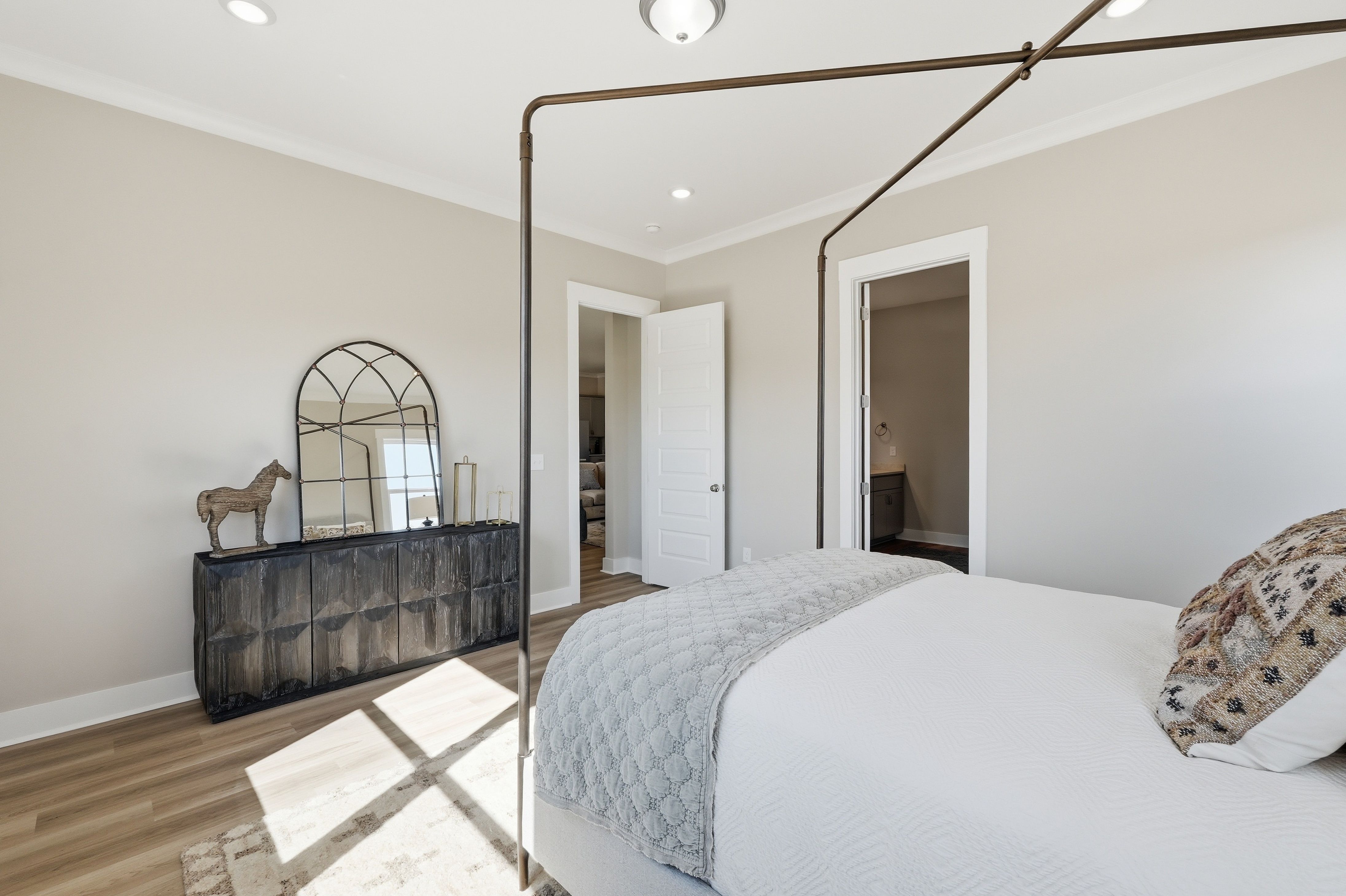 Spacious bedroom at The Meadows at Hampton Cove in Owens Cross Roads AL with four-poster bed, arched mirror, hardwood floors