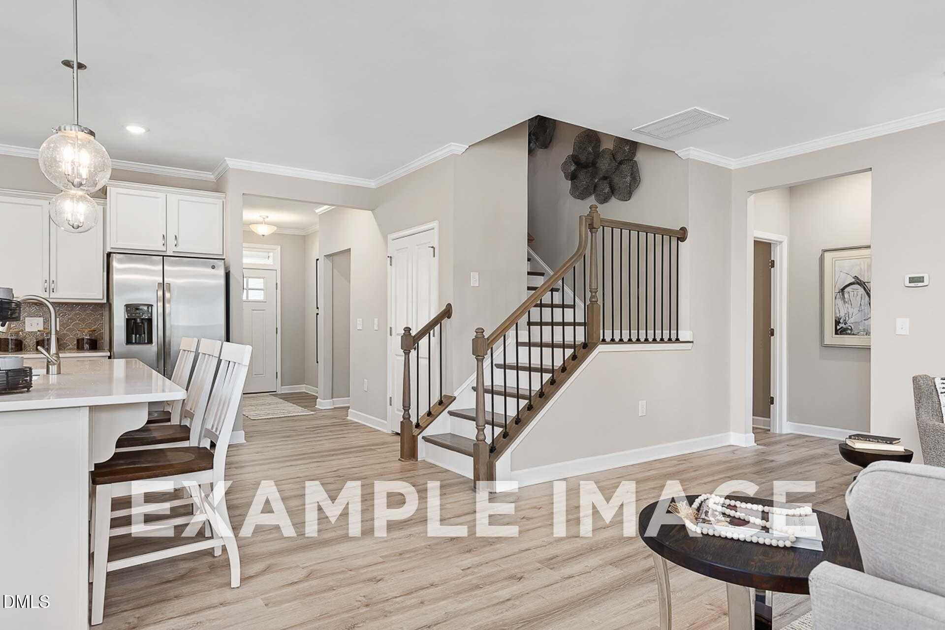 Modern open-concept kitchen with white cabinets, island bar, stainless appliances, and curved staircase in Davidson Homes The Ash B, Lillington, NC
