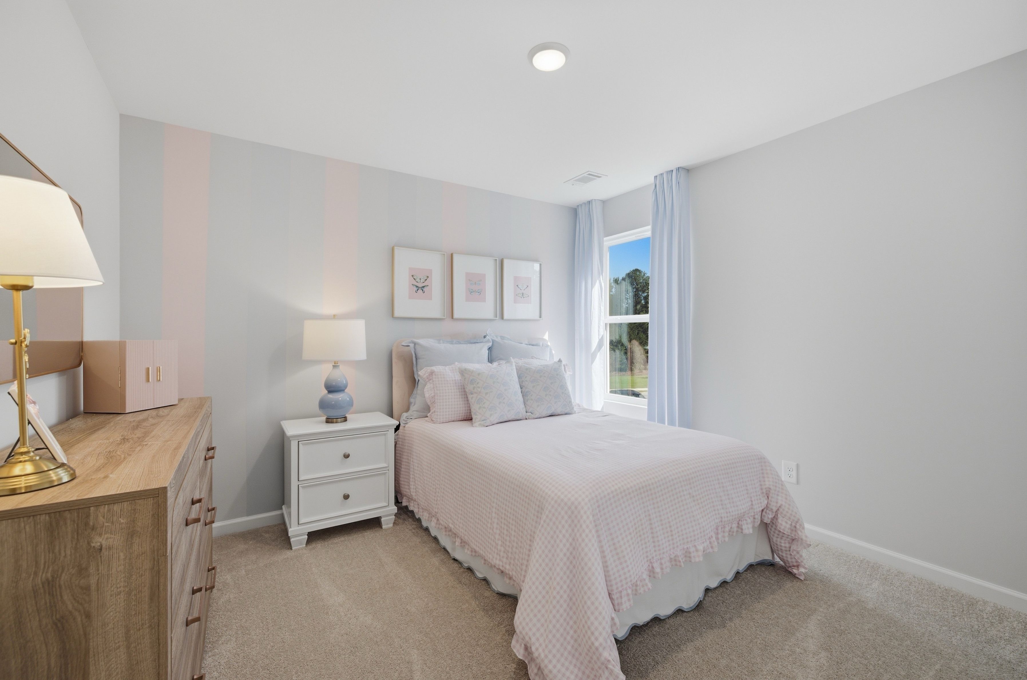 Bright pastel bedroom with pink gingham bedding and butterfly art at Greene Farm by Davidson Homes in Cartersville, GA