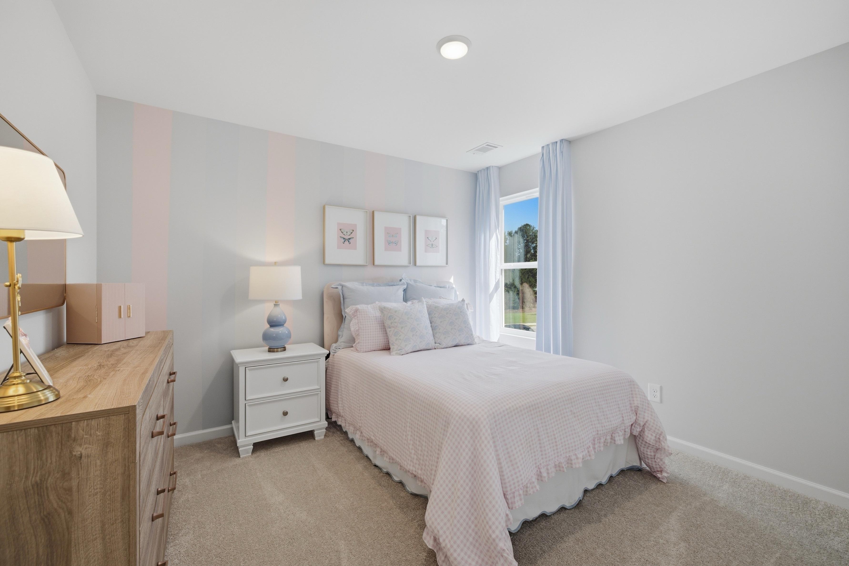 Bright pastel bedroom with pink gingham bedding and butterfly art at Greene Farm by Davidson Homes in Cartersville, GA
