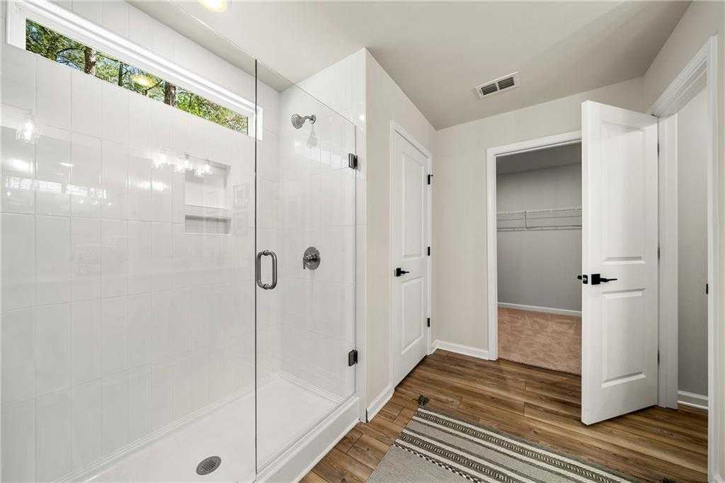 Modern master bathroom featuring frameless glass shower, white tile, and adjacent walk-in closet in Davidson Homes The Hickory B, Riverwood, Dallas, Georgia